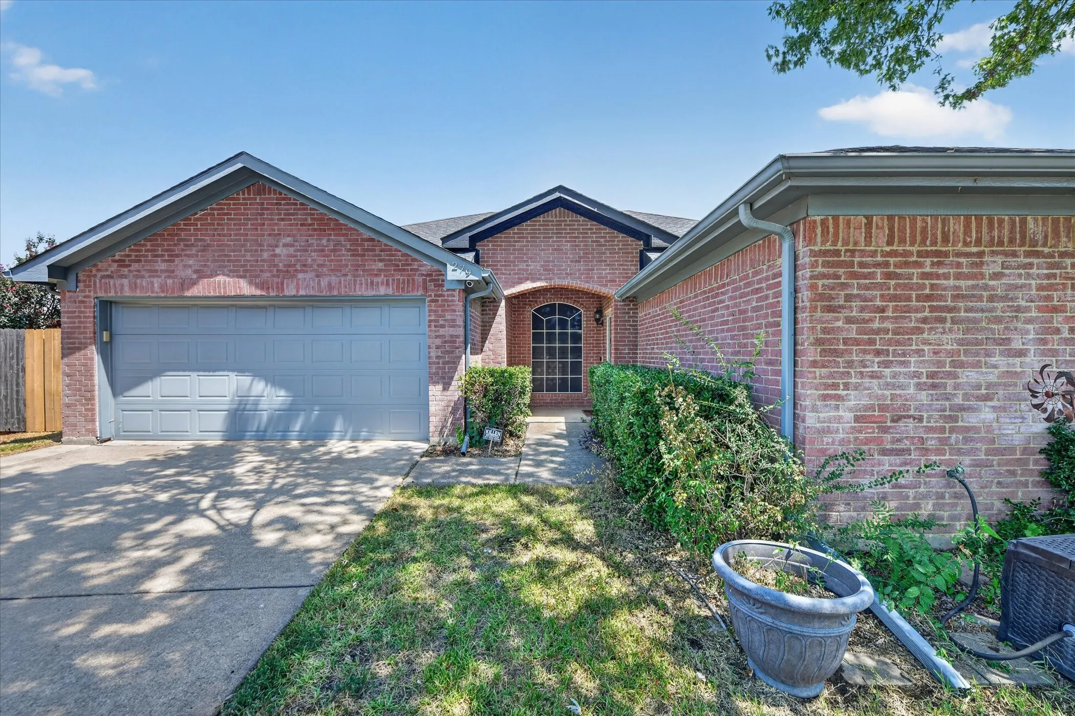Brick exterior with gray trim, attached garage with panel door, arched entry, and concrete driveway