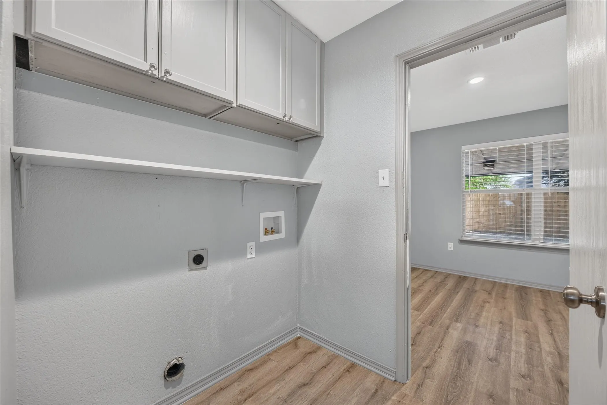 Laundry area featuring wood-finish flooring, wall-mounted shelving, and upper cabinetry