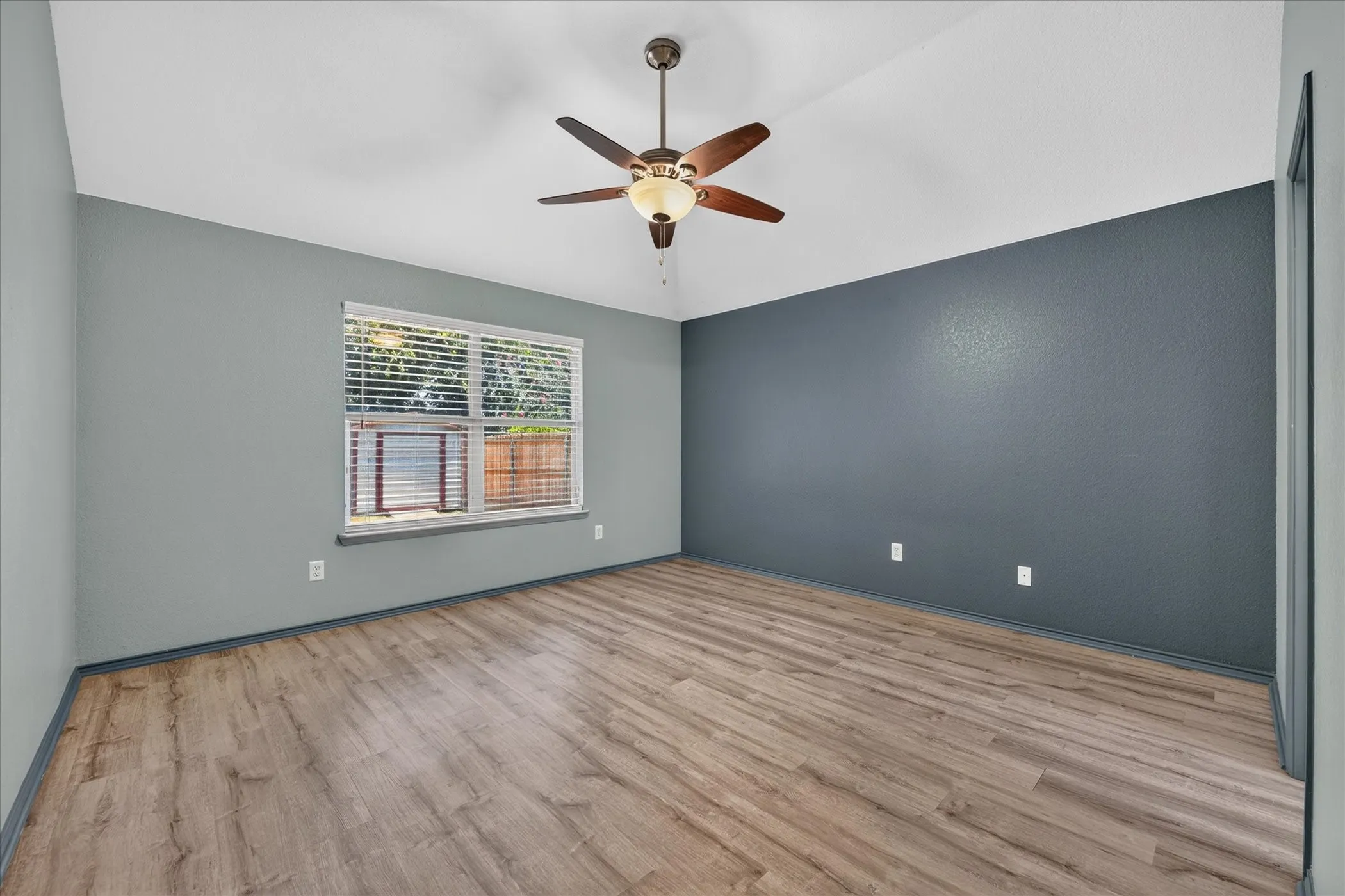 Vaulted ceiling with a ceiling fan, wood-finish flooring, and a window with blinds