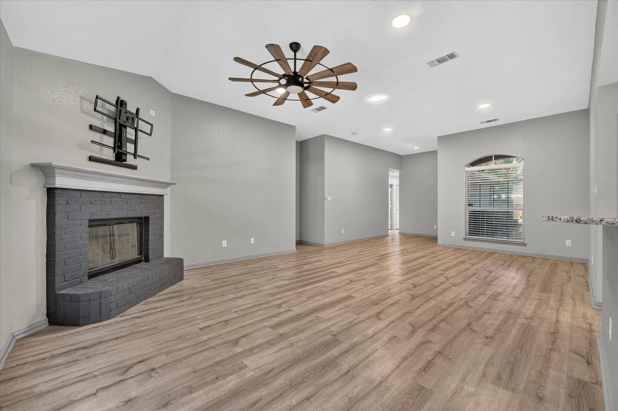 Wood-finish flooring, vaulted ceiling, recessed lighting, ceiling fan, and brick fireplace with mantel