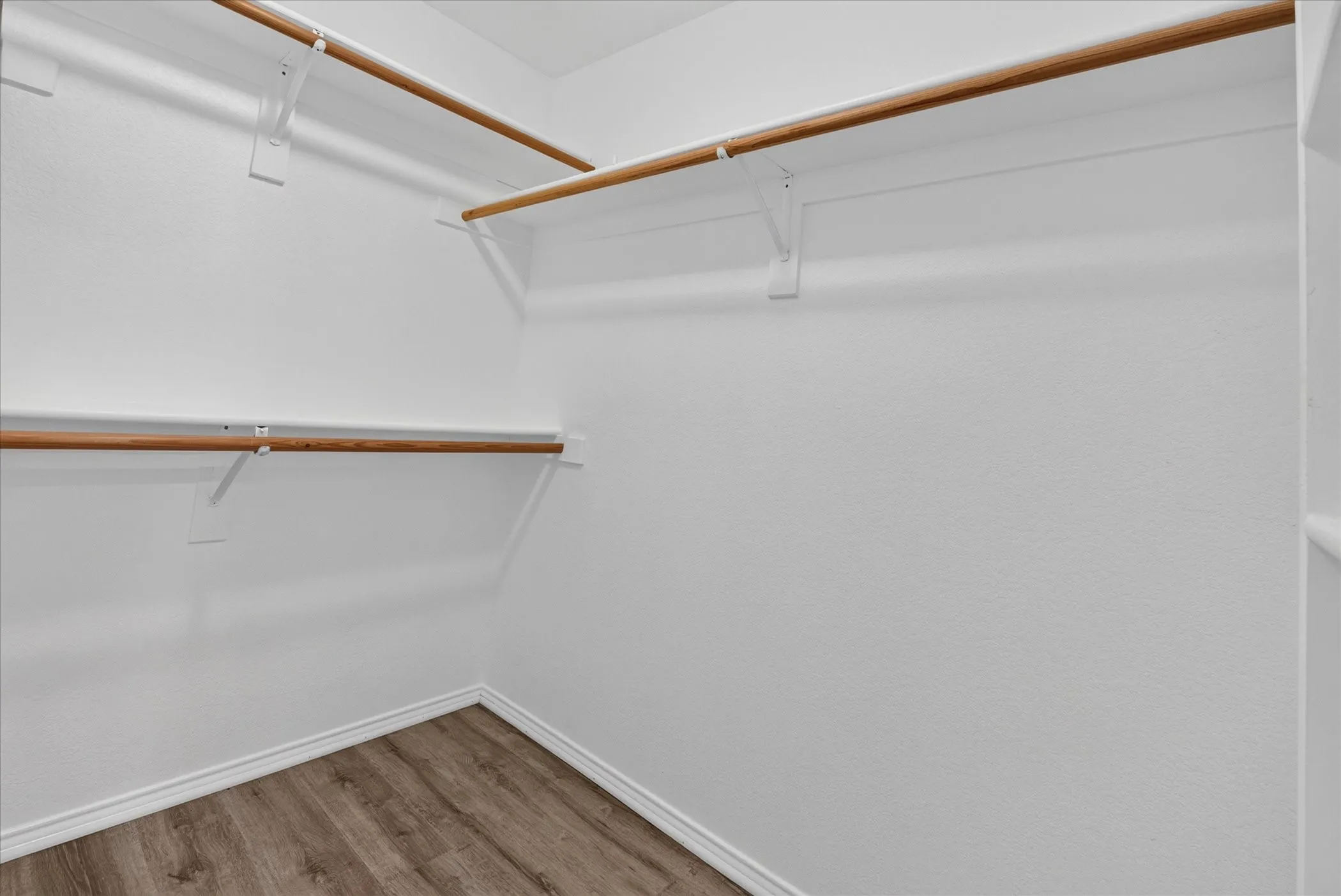Walk-in closet featuring wood-finish flooring and multiple shelving units with hanging rods