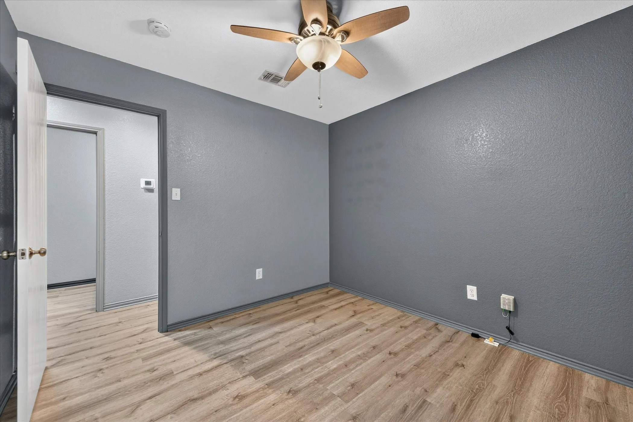 Wood-finish flooring with a ceiling fan and textured walls