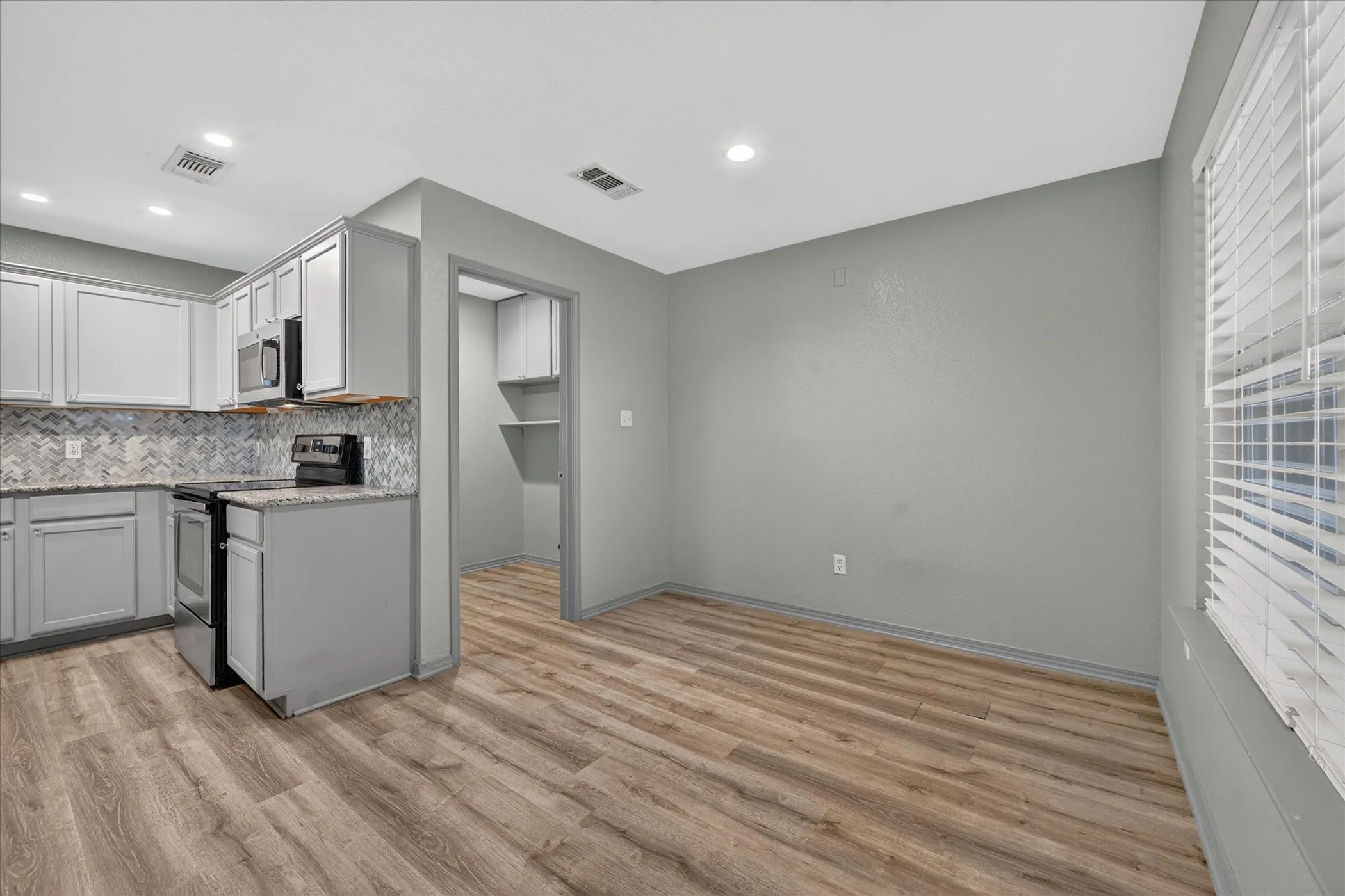Kitchen featuring gray cabinetry, stainless steel appliances, patterned tile backsplash, and wood-finish flooring