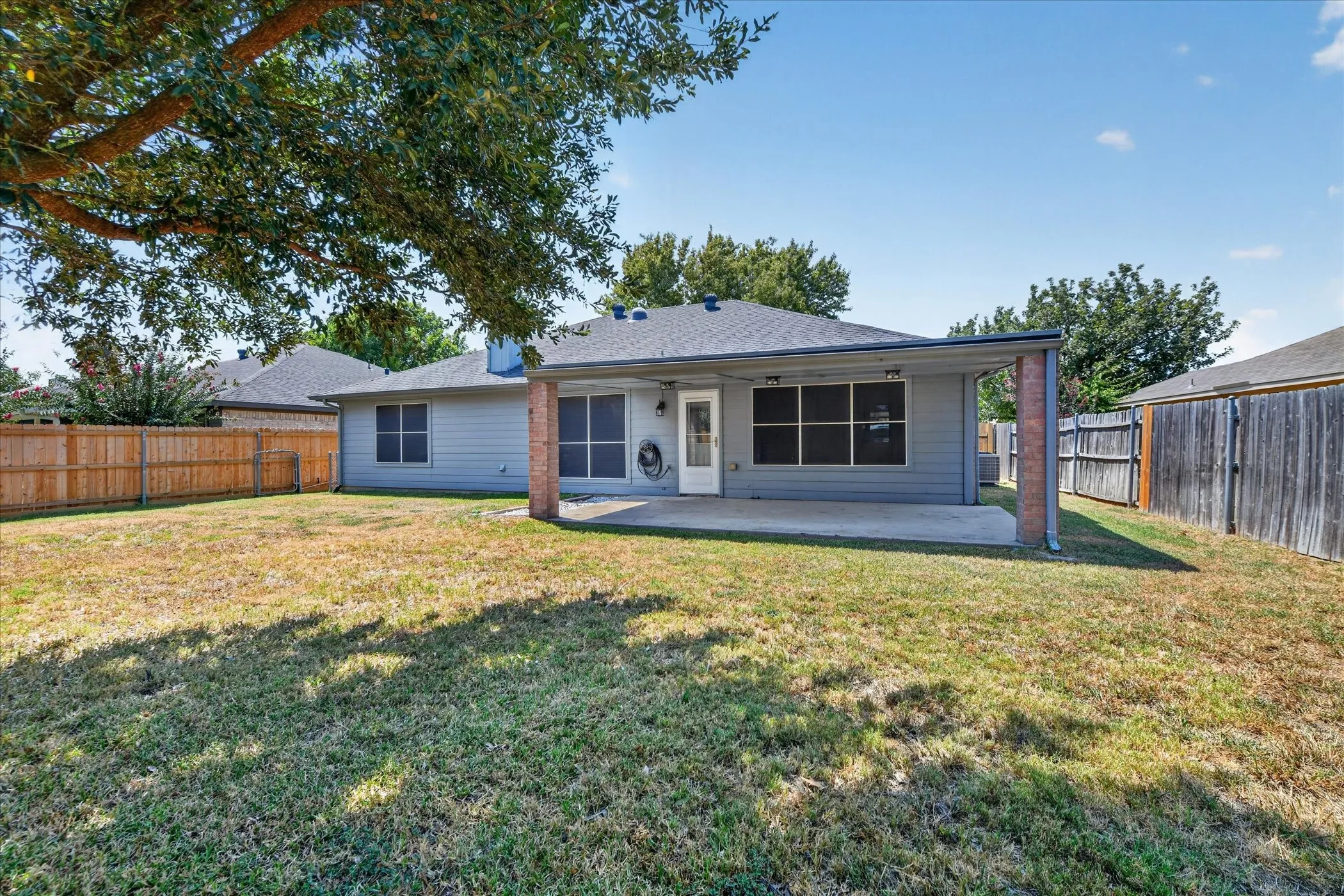Expansive backyard featuring a covered patio with brick columns, a substantial mature tree, and wood fencing