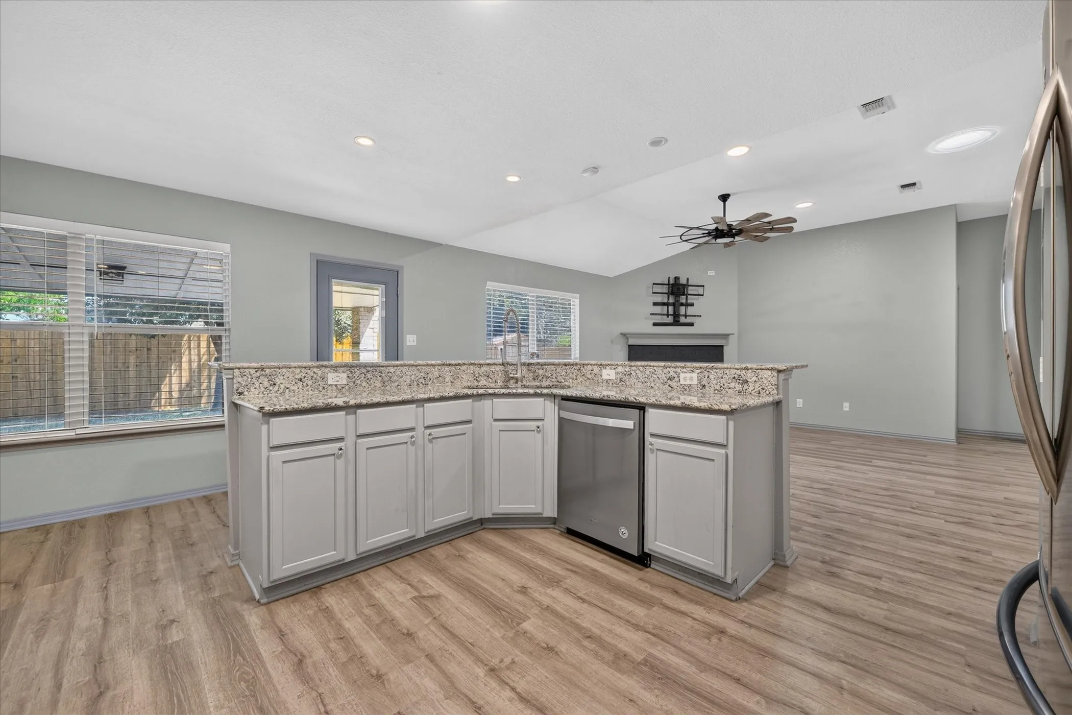 Modern kitchen featuring white cabinetry with a granite-topped island, stainless steel appliances, recessed ceiling lighting, and a ceiling fan