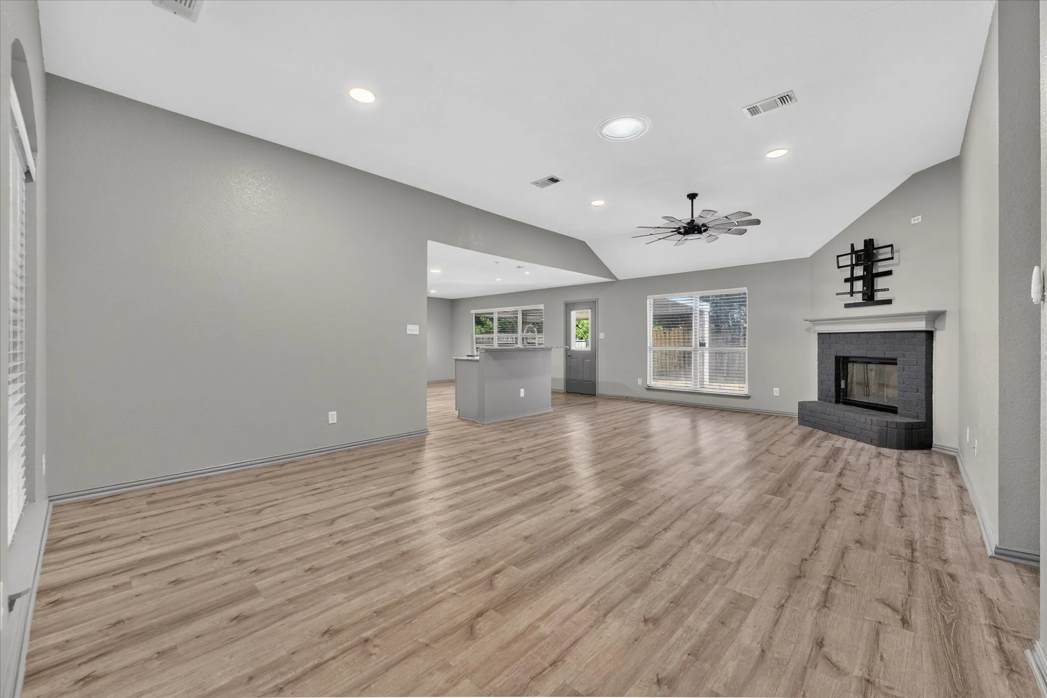 Spacious living area featuring wood-finish flooring, a fireplace with a dark stone surround, vaulted ceilings, recessed lighting, and a ceiling fan