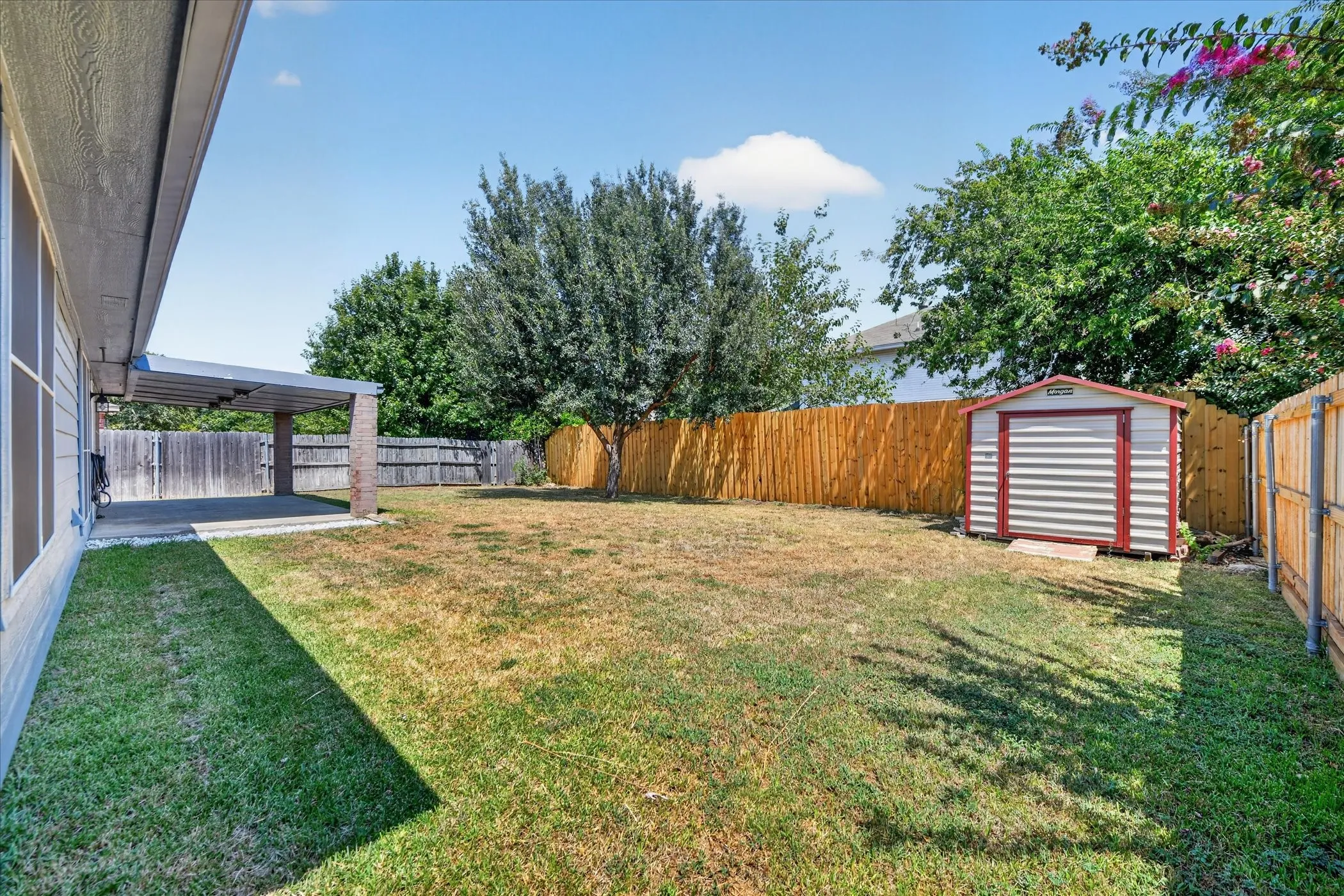 Expansive outdoor space featuring a covered patio, a storage shed, and perimeter fencing