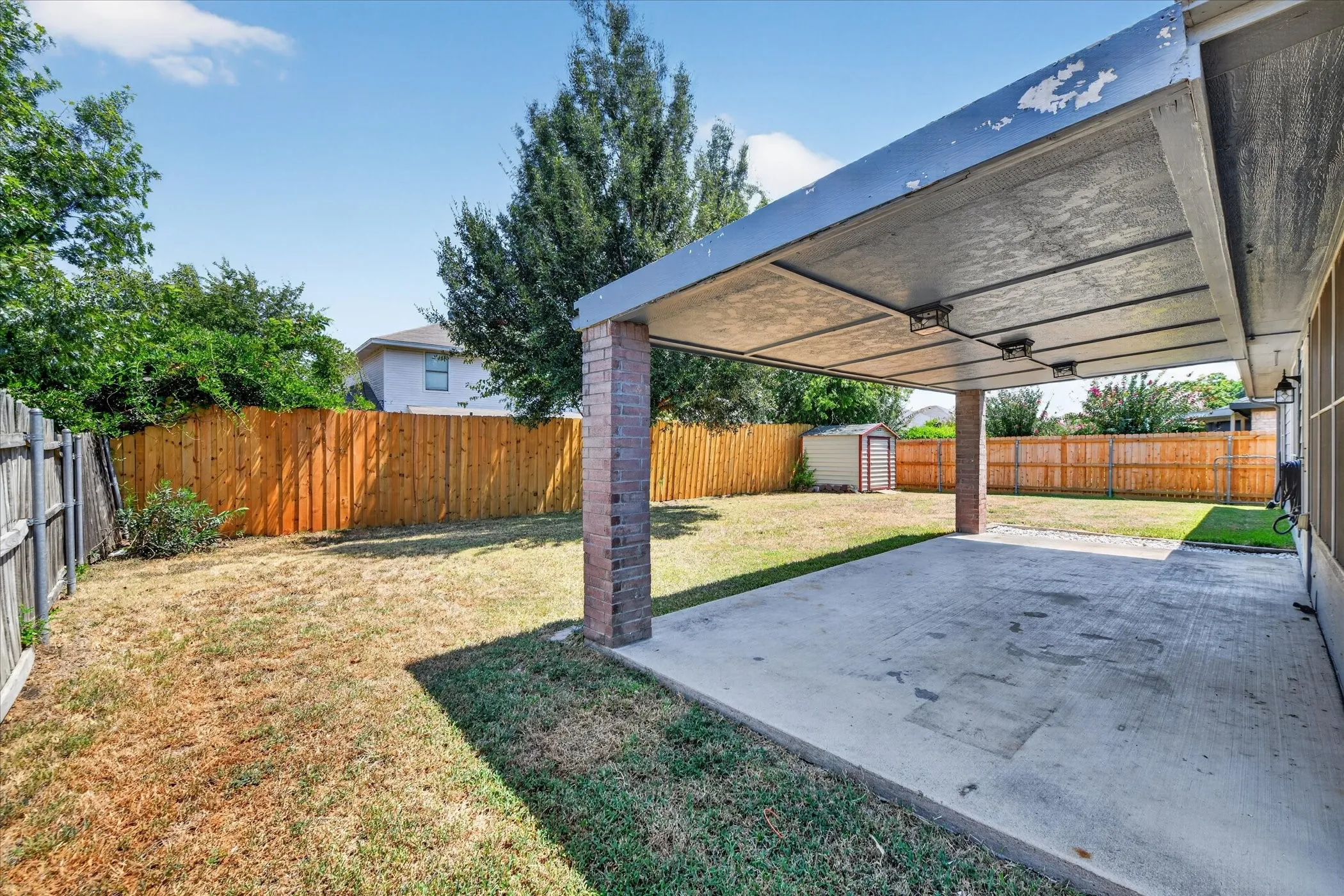 Covered patio with a concrete surface, brick columns, and a fully fenced backyard featuring a storage shed