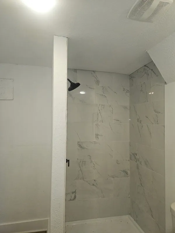 Shower with large format marble-look tile surround, matte black shower fixtures, and recessed lighting