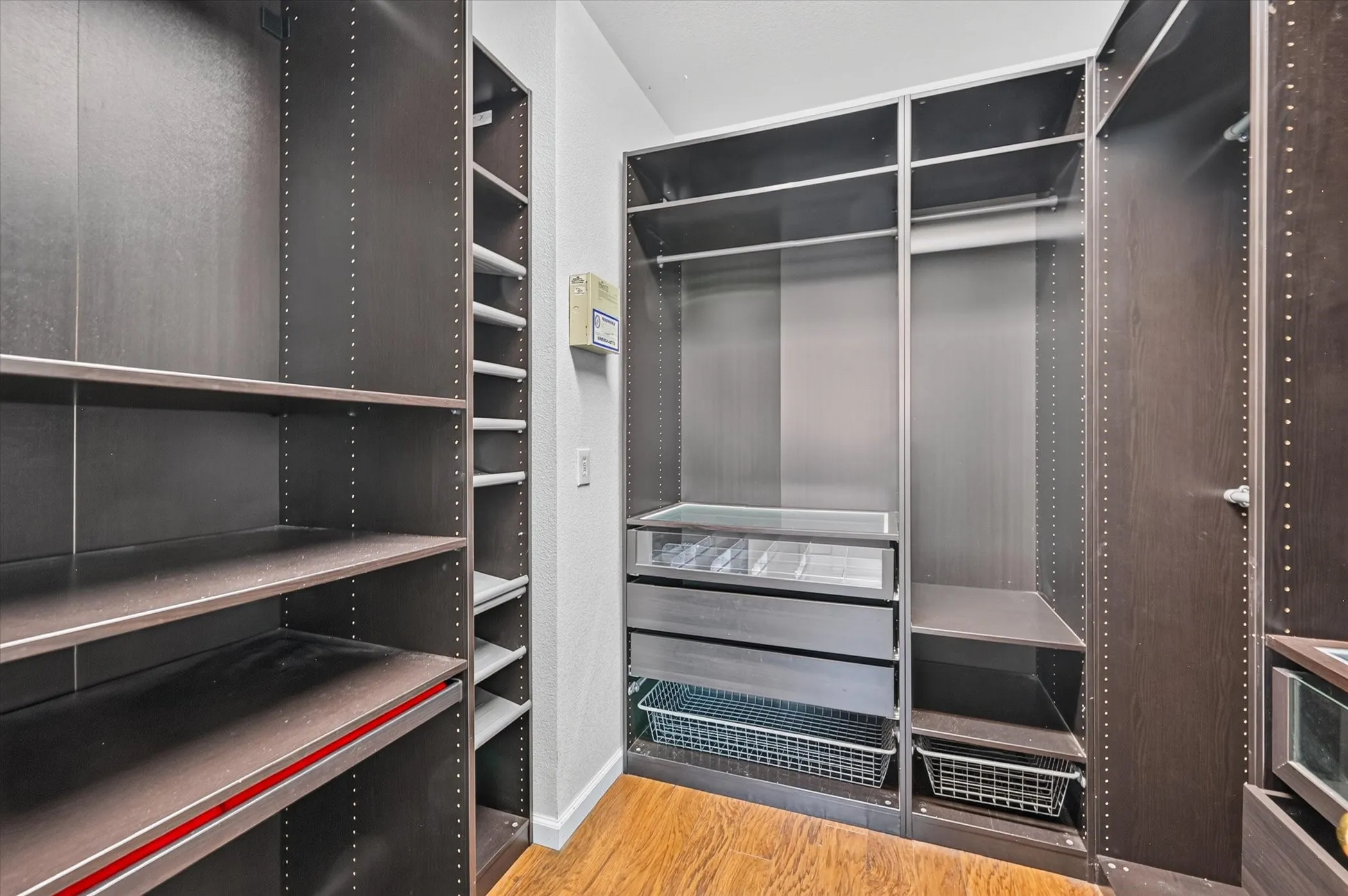 Custom closet system featuring wood-finish flooring, multiple shelving units, integrated drawers, and wire baskets