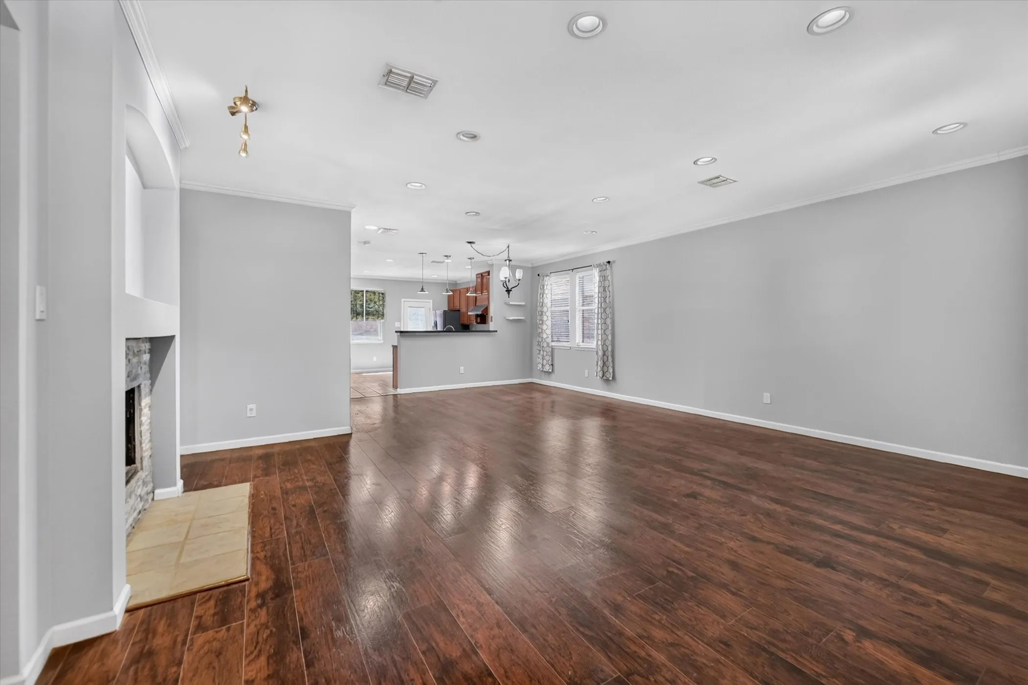 Wood-finish flooring throughout, recessed ceiling lighting, a stone-clad fireplace with a hearth, and crown molding