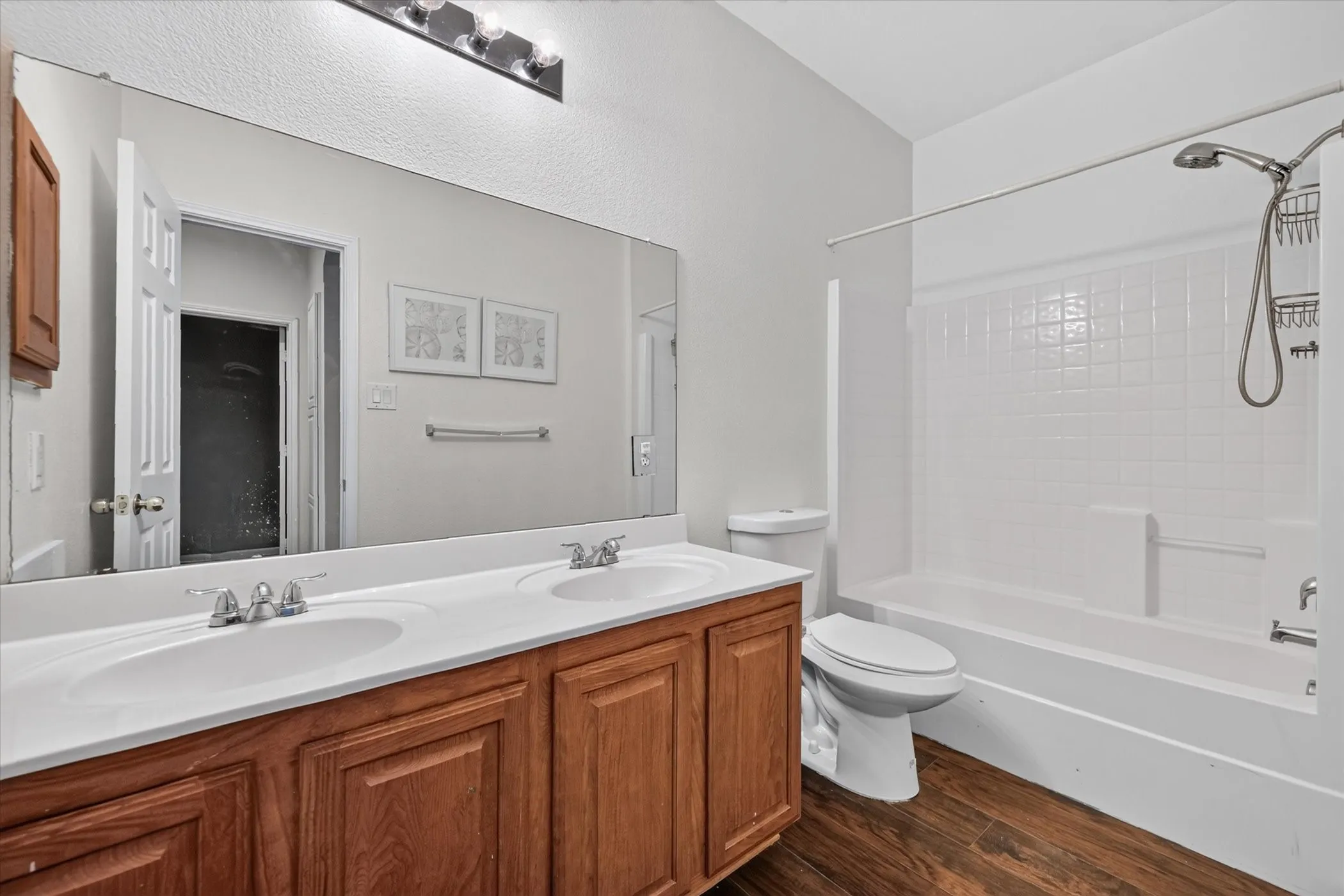 Dual vanity with integrated sinks, wood-finish cabinetry, a full-width mirror, and overhead lighting