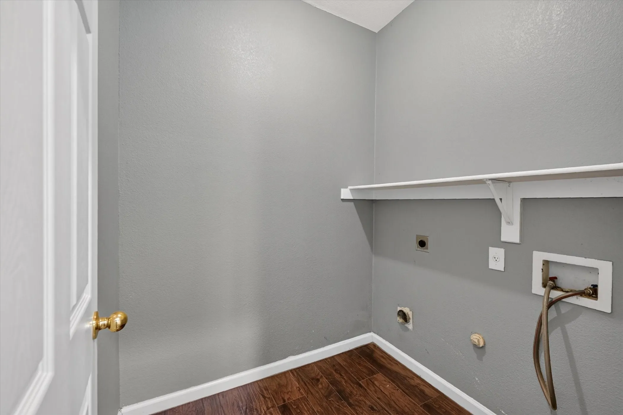 Utility area featuring wood-finish flooring, a white paneled door, and a built-in wall shelf