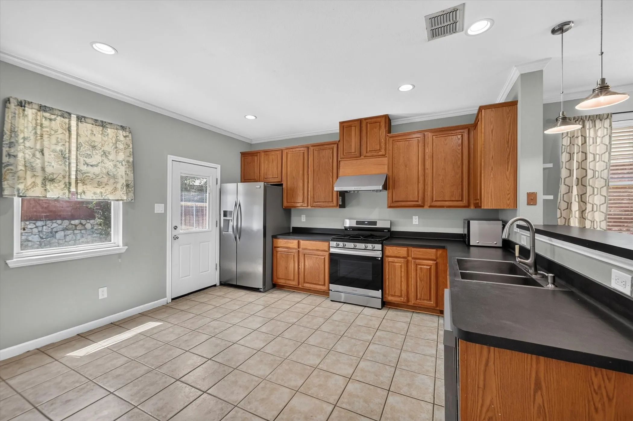 Kitchen featuring wood cabinetry, stainless steel appliances, dark countertops, a double basin sink with a gooseneck faucet, and tile flooring
