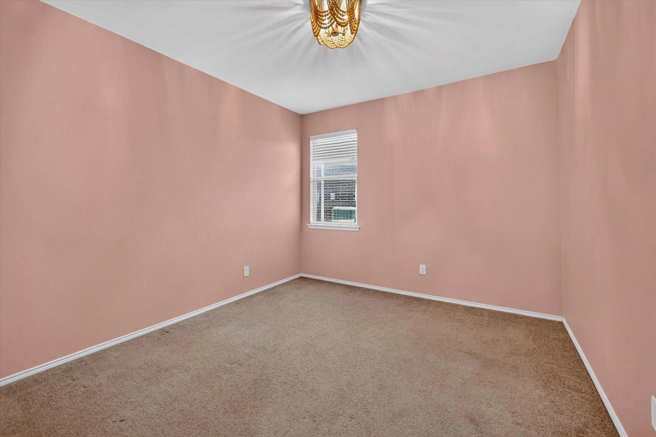 Neutral carpet flooring, a single window with blinds, and an overhead light fixture