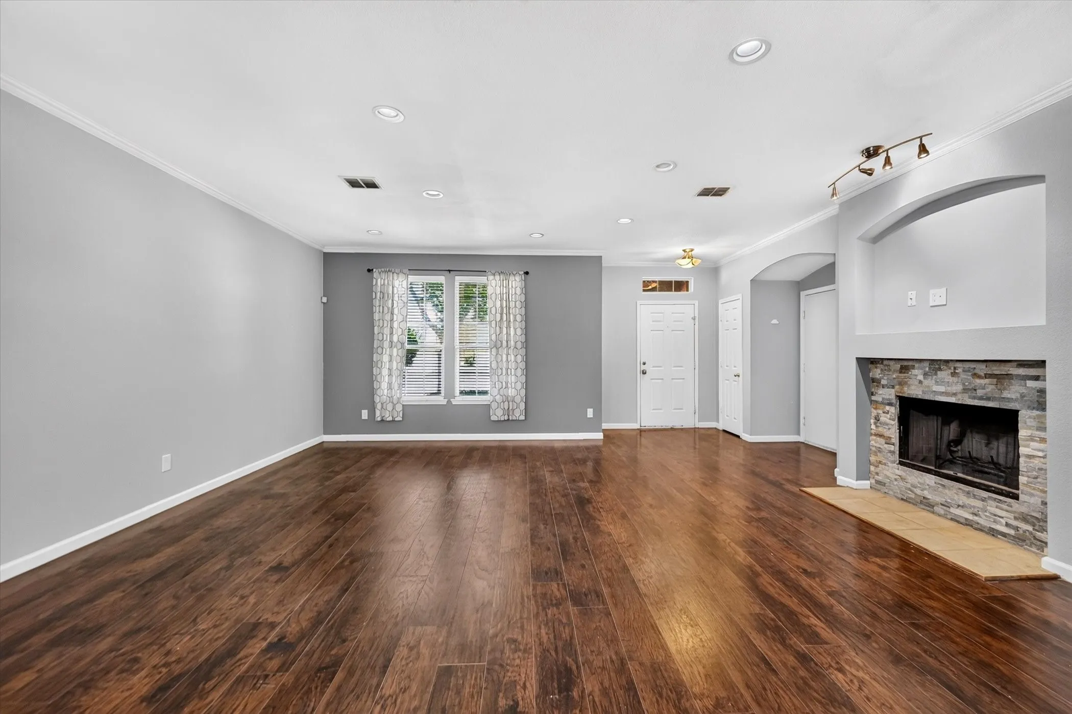 Spacious living area featuring wood-finish flooring, recessed lighting, and a stacked stone fireplace with an arched alcove
