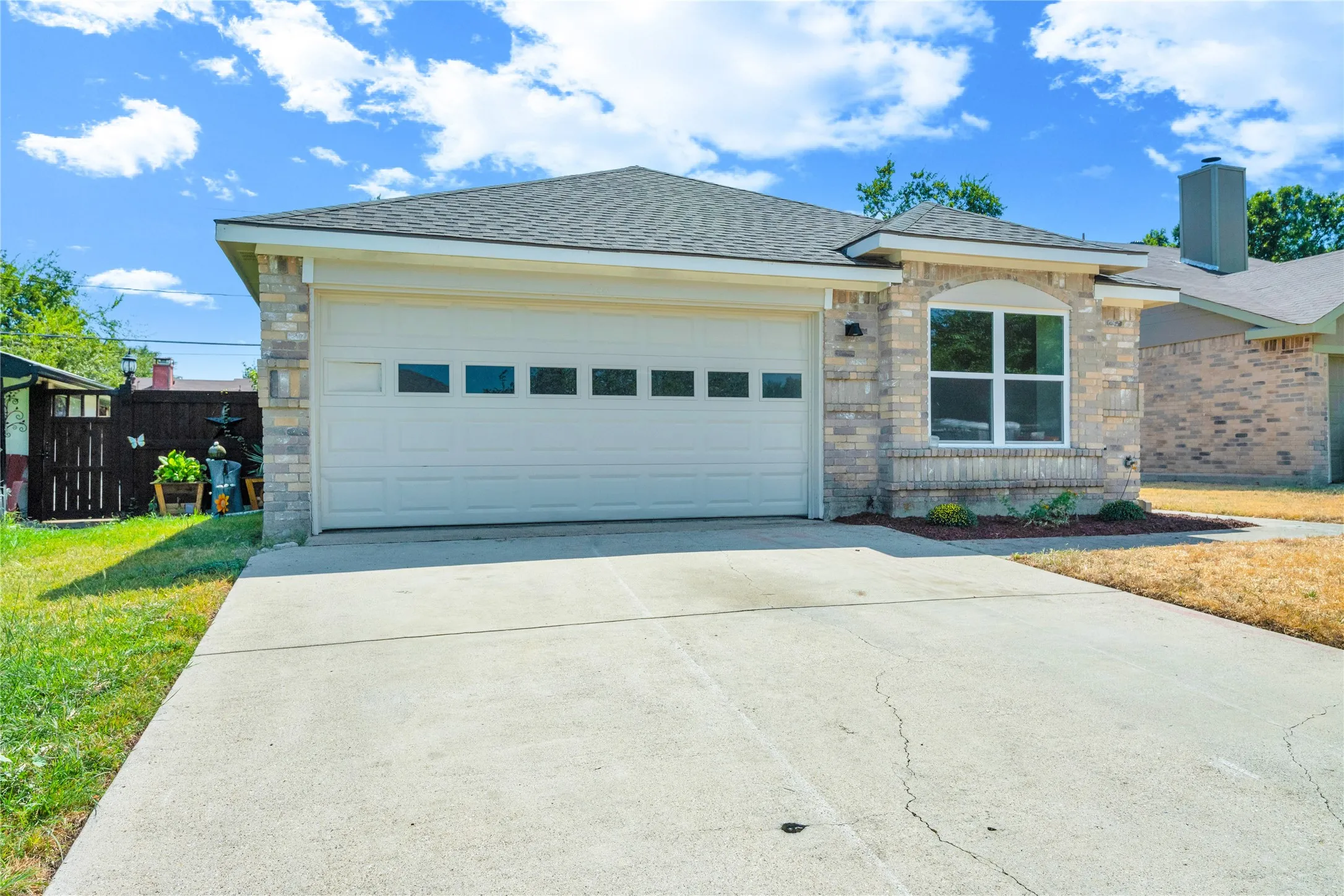 Brick exterior with an arched window accent, attached garage with window inserts, concrete driveway, and a fenced side yard