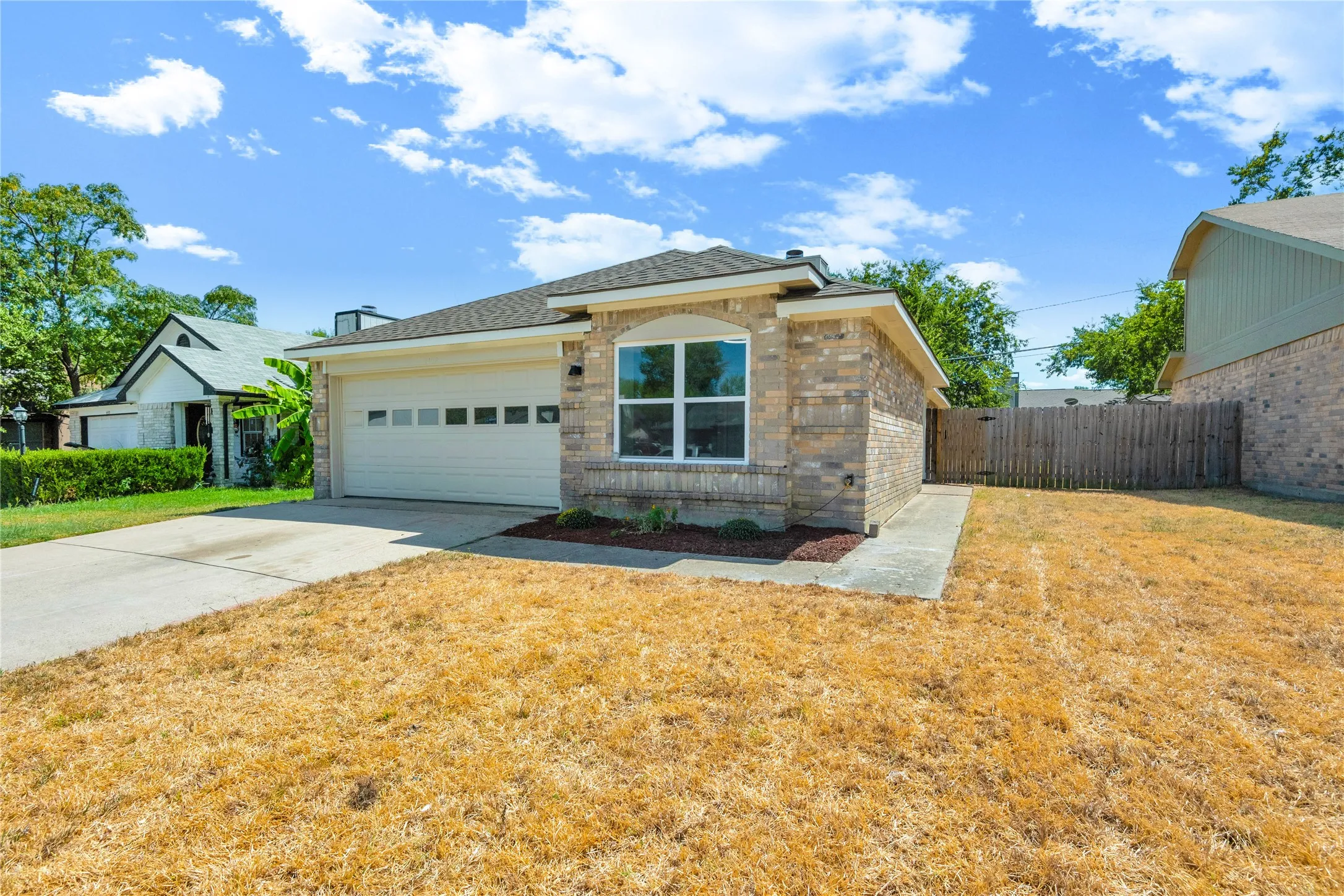 Brick exterior with an arched window, attached garage, concrete driveway, and side yard with a wooden privacy fence