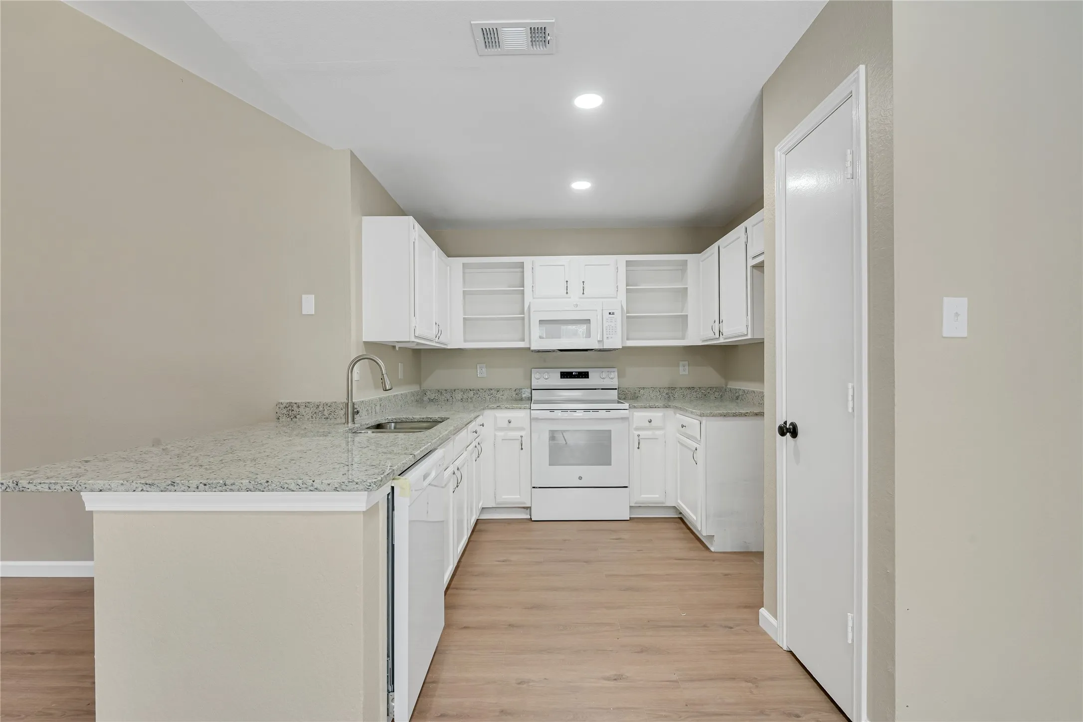 White cabinetry with clear glass door accents, stainless steel gooseneck faucet, light-toned countertops, integrated white appliances, and wood-finish flooring