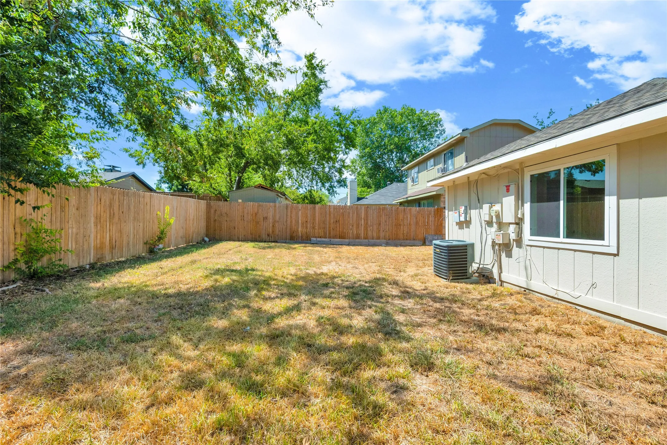 Spacious backyard with a wood privacy fence, featuring a single window on the exterior wall