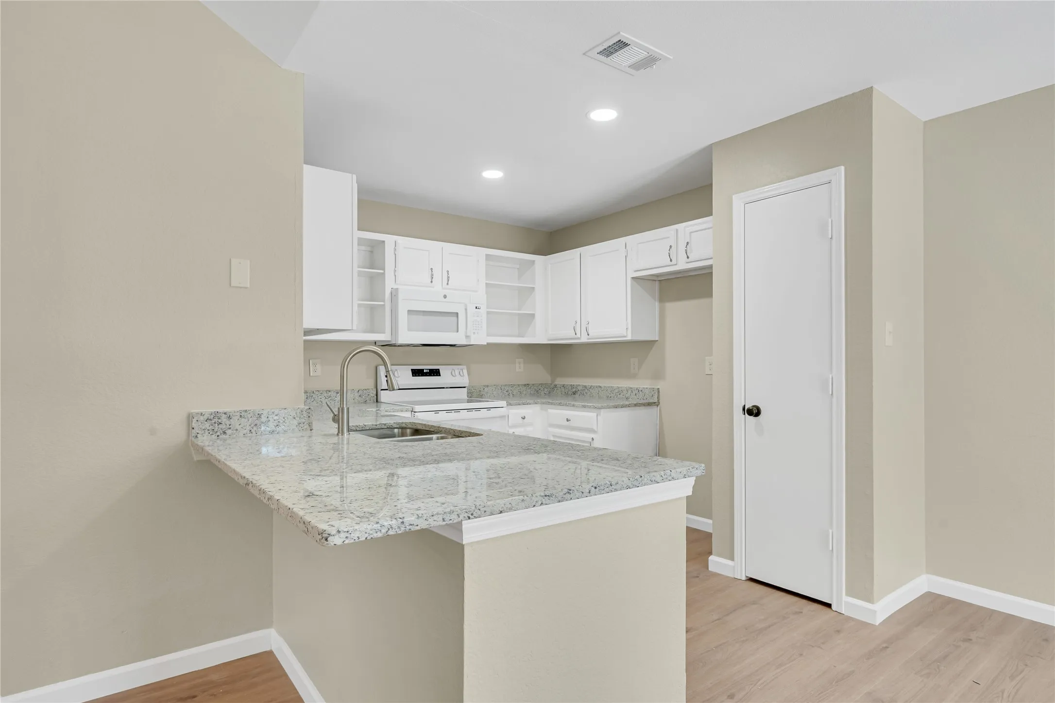Kitchen featuring a breakfast bar with stone countertops, white cabinetry, stainless steel sink with gooseneck faucet, and wood-finish flooring
