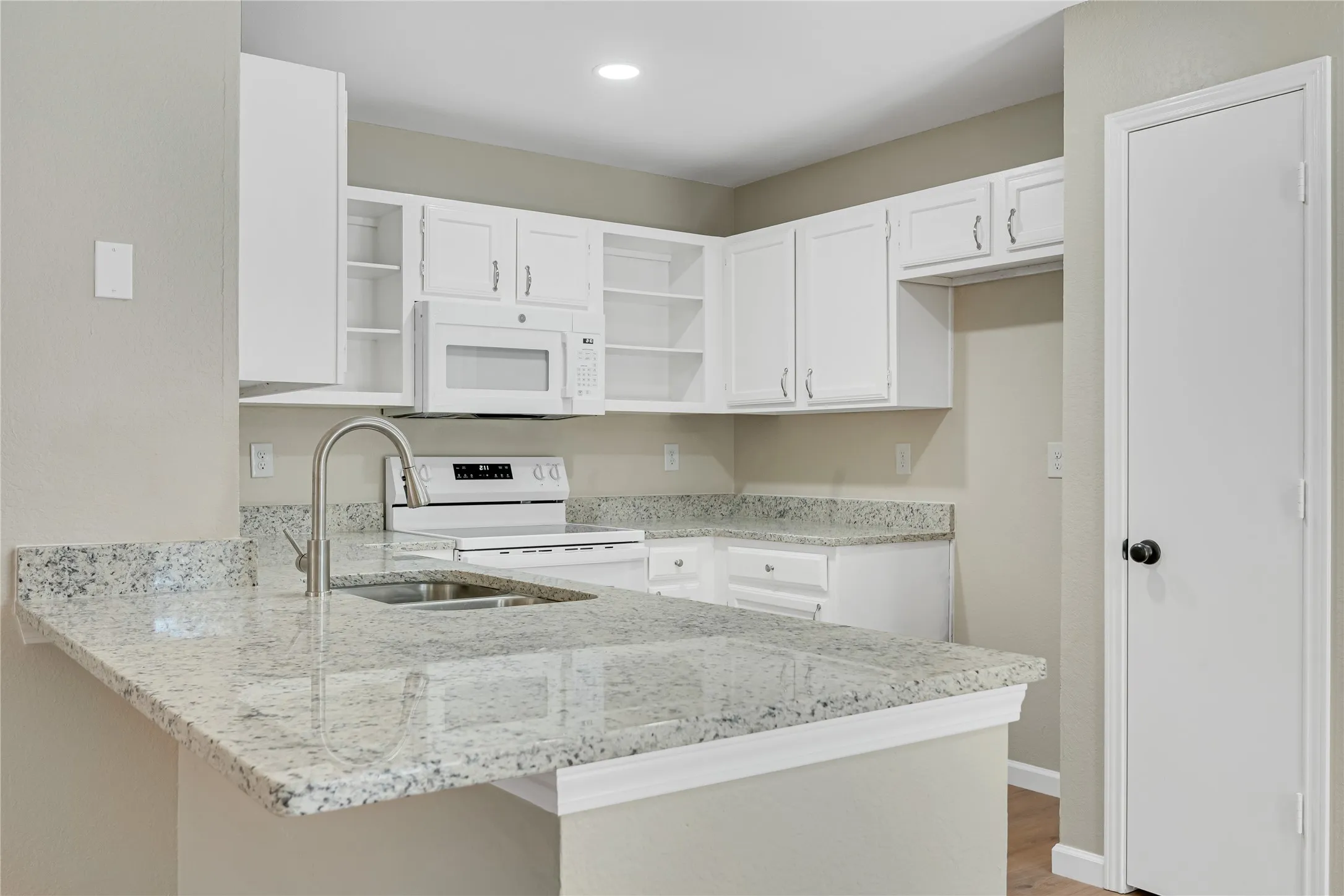Kitchen featuring white cabinetry, light-toned countertops, a stainless steel sink with a gooseneck faucet, a built-in microwave, and a white electric range