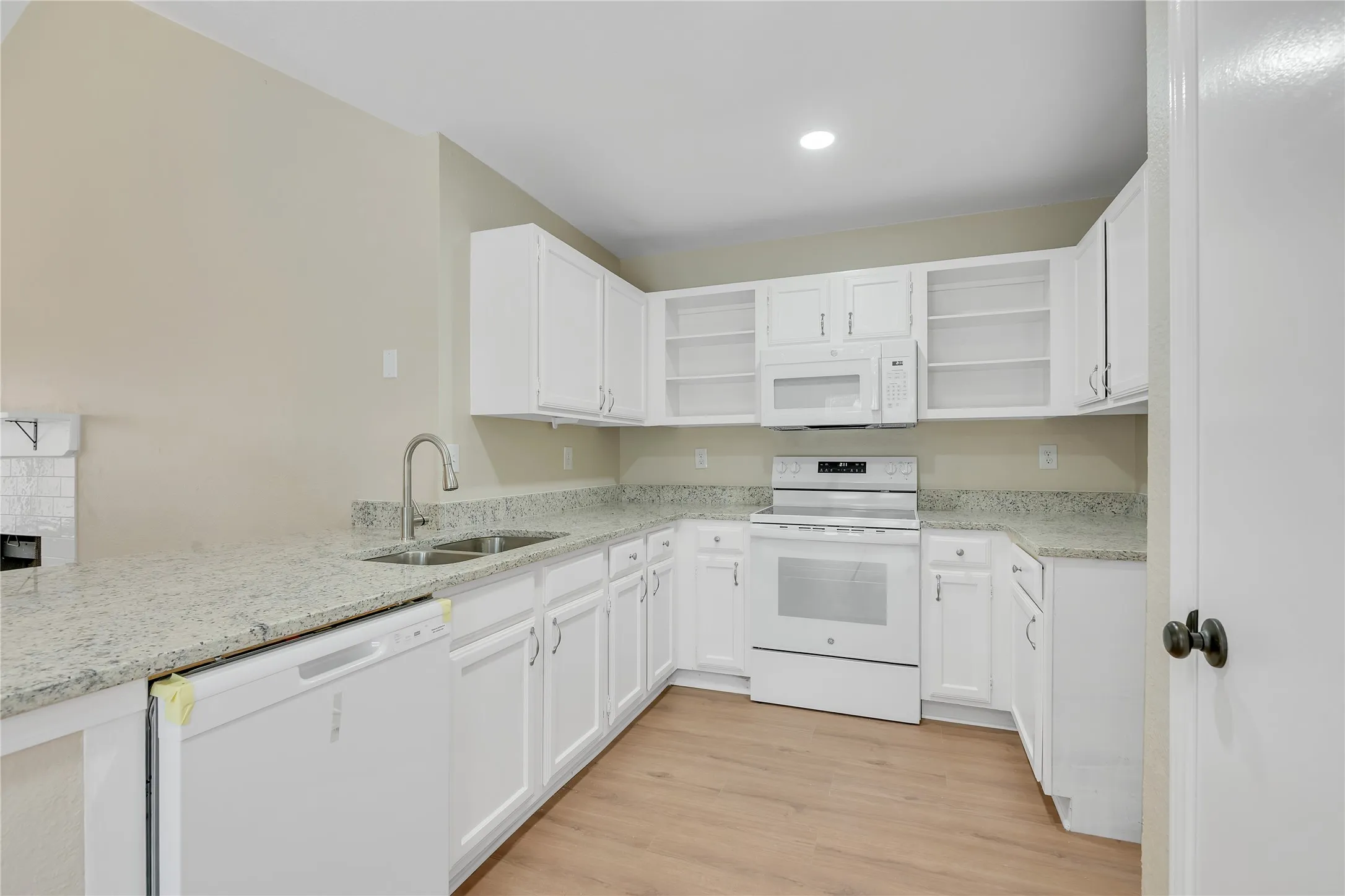 Kitchen featuring white cabinetry, light-toned countertops, stainless steel sink, white electric range, and wood-finish flooring