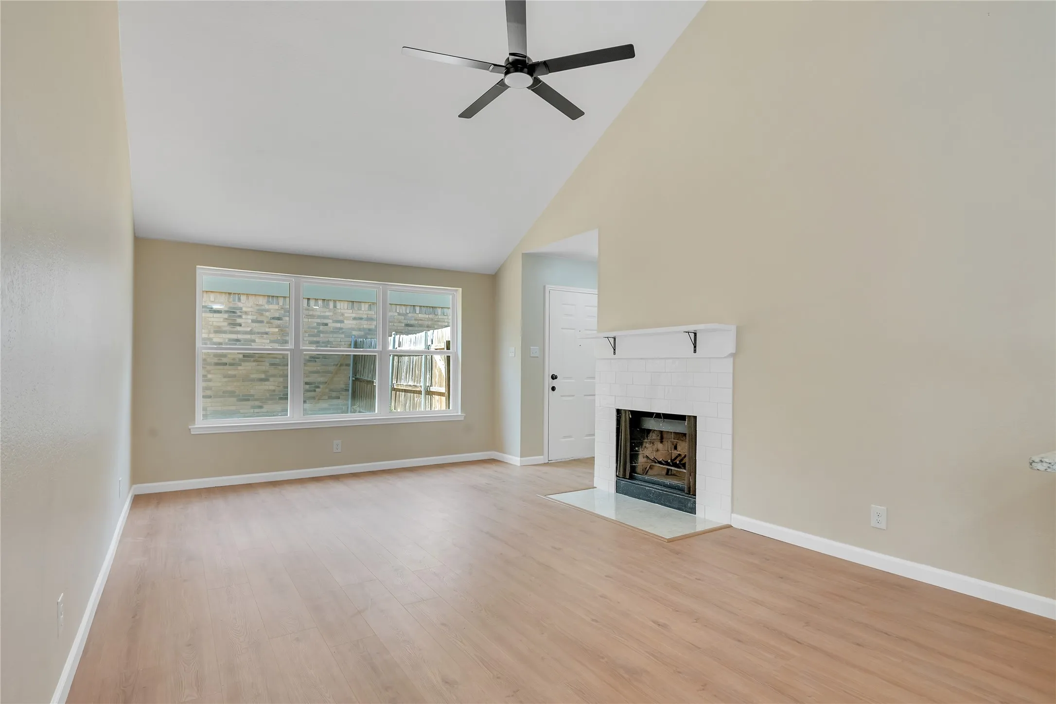 Vaulted ceilings, wood-finish flooring, white brick fireplace with mantel, and large windows