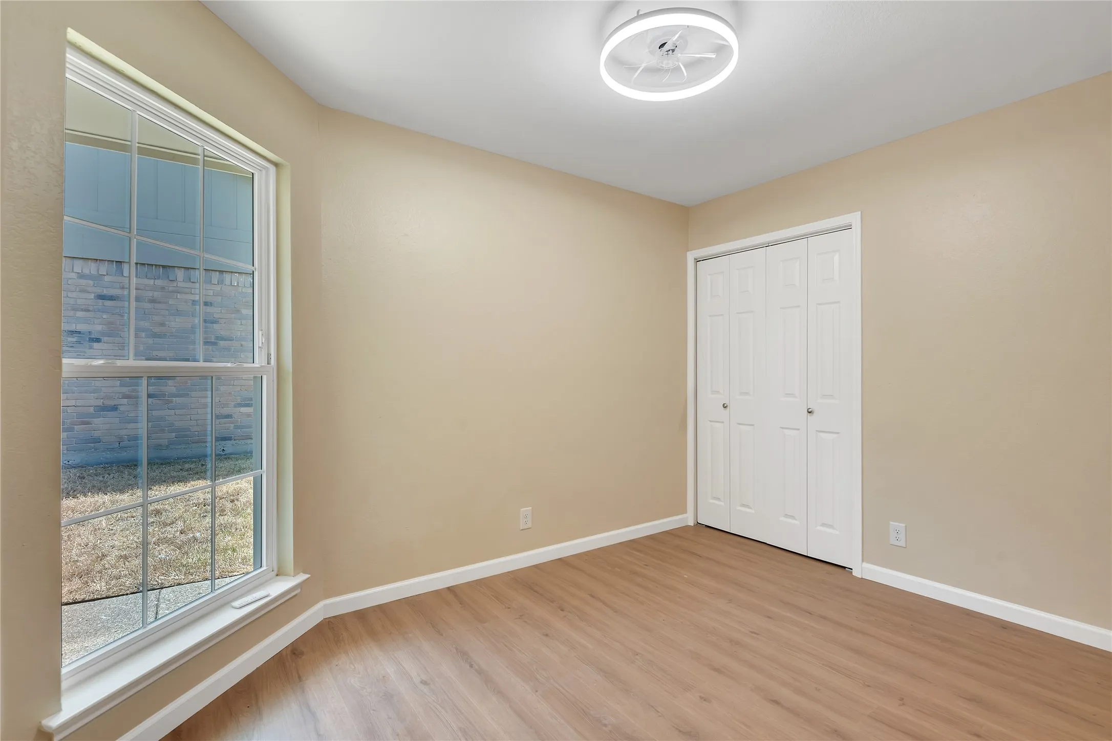 Light-filled room featuring a large window, bi-fold closet doors, wood-finish flooring, and a modern ceiling fixture