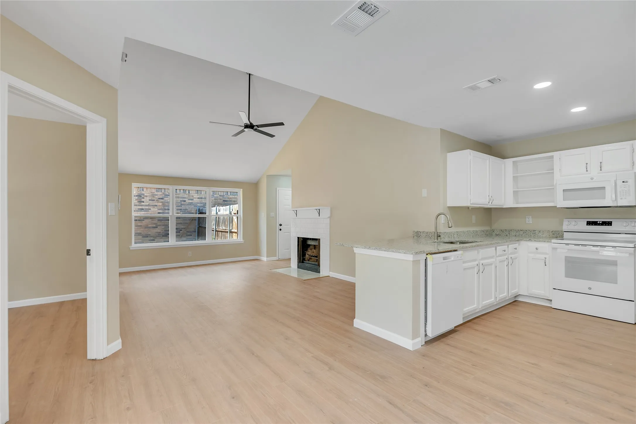 Vaulted ceilings, wood-finish flooring, fireplace, kitchen island with sink, and white cabinetry