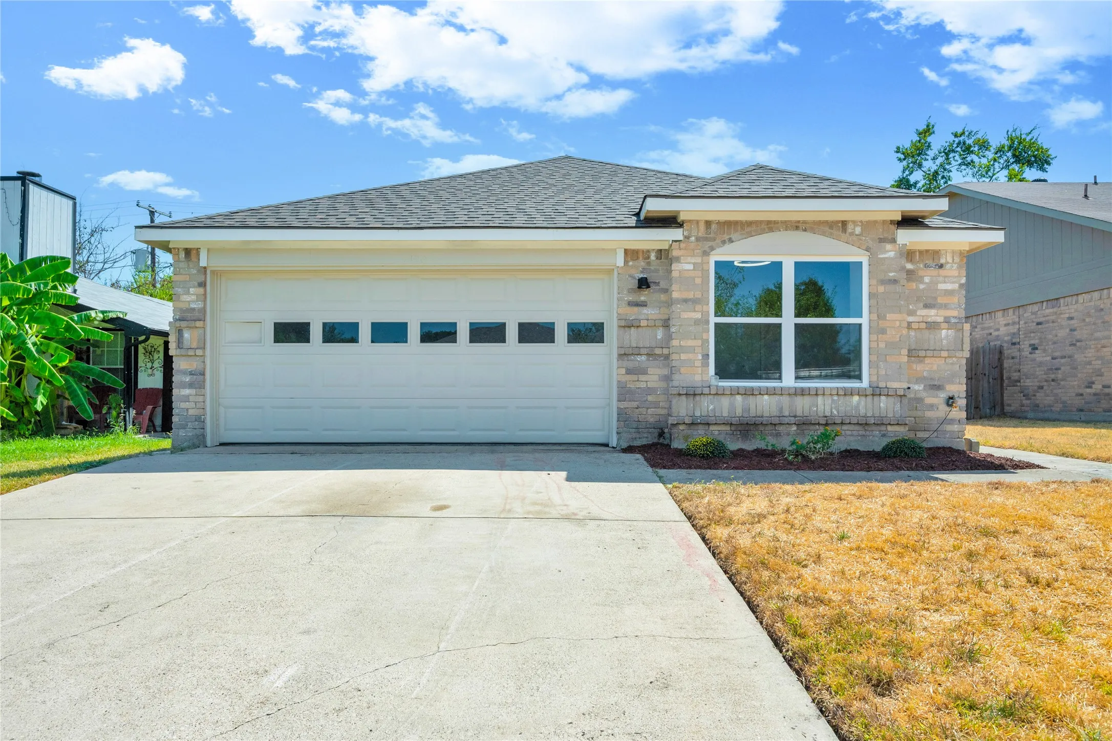 Brick facade with arched window detail, attached garage with window inserts, and asphalt shingle roof