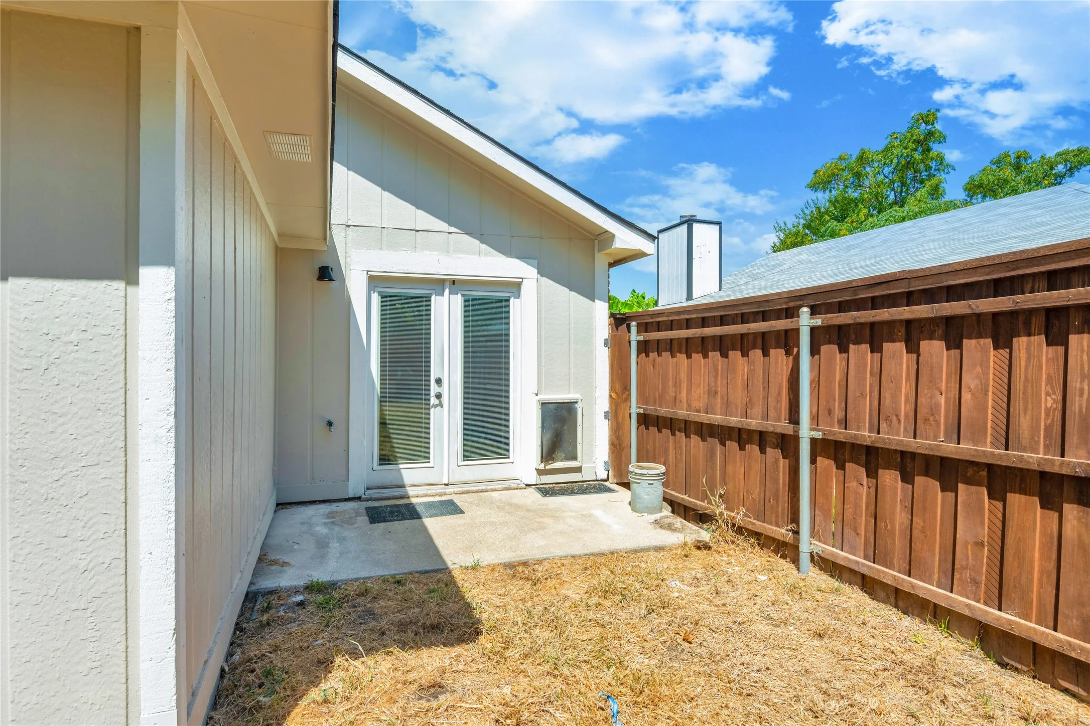 Private outdoor area featuring a wood fence, concrete patio, and exterior lighting