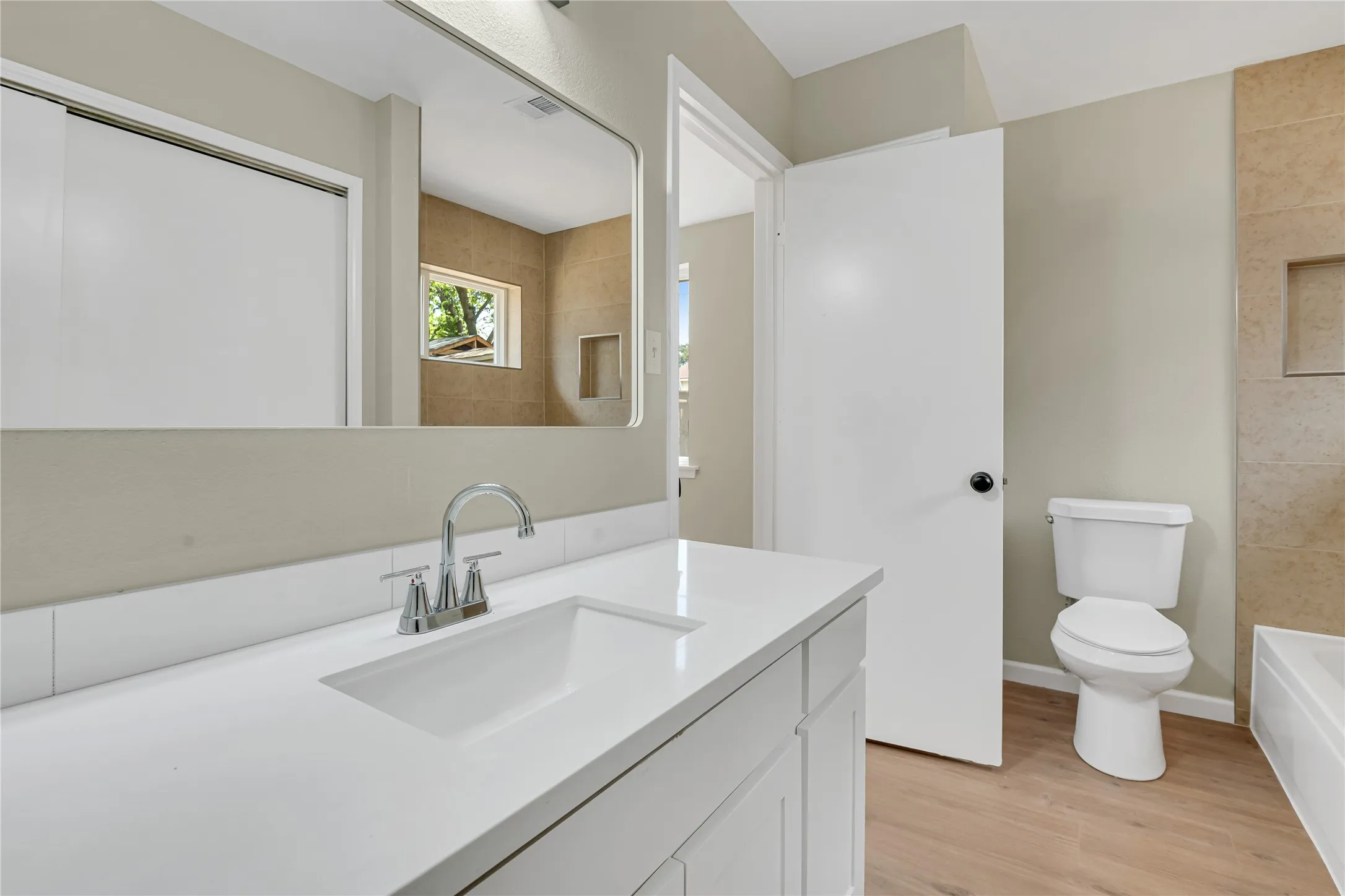 White vanity with an integrated rectangular sink, chrome faucet, and expansive wall mirror