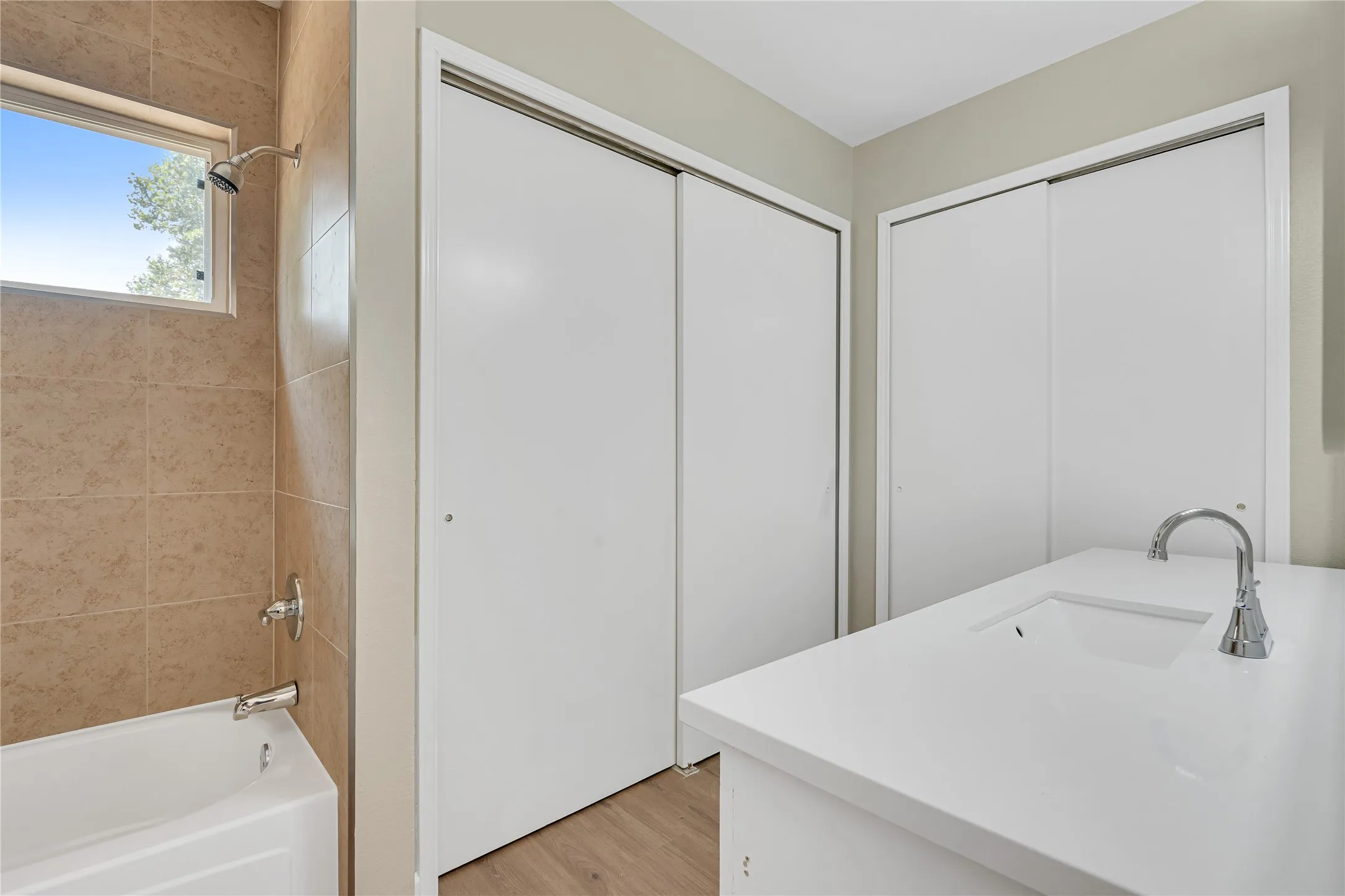 White bathtub with chrome fixtures, tiled shower surround, and a clear window