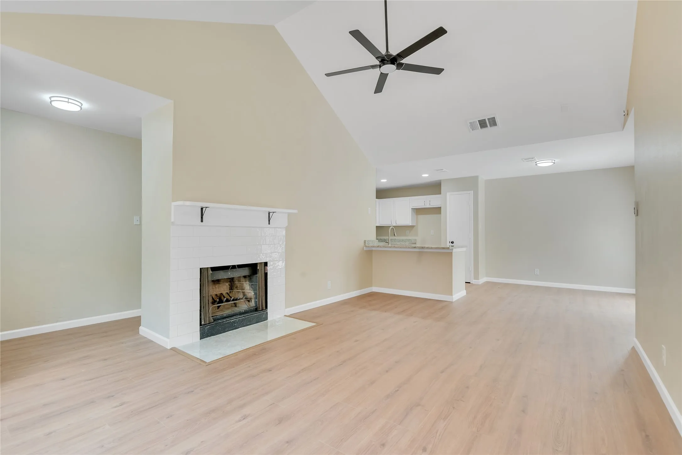 Vaulted ceiling great room with wood-finish flooring, a tiled fireplace, and a ceiling fan