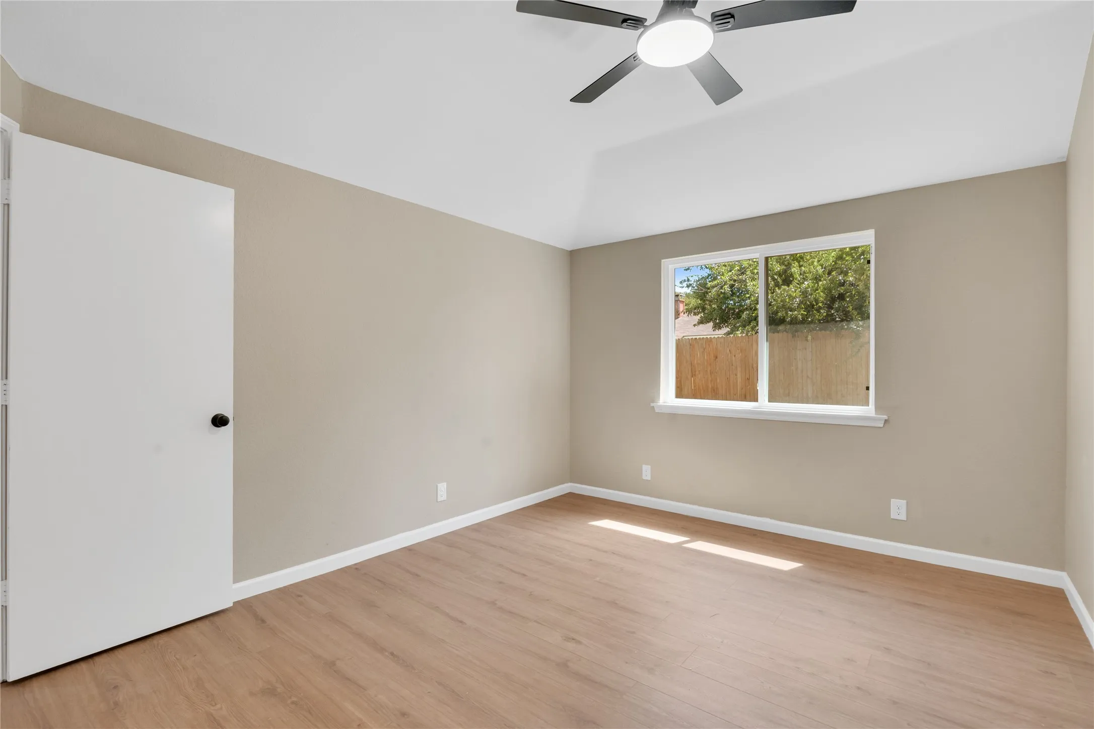 Vaulted ceiling with a flush-mount ceiling fan, wood-finish flooring, and a double window