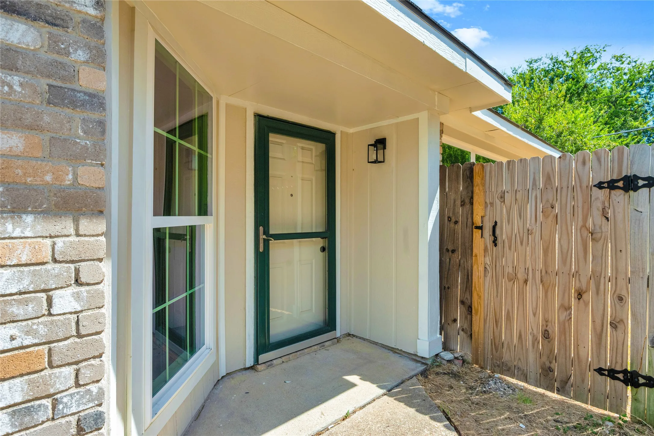 Brick facade with a bay window, covered entry, and wood fence with wrought iron hardware