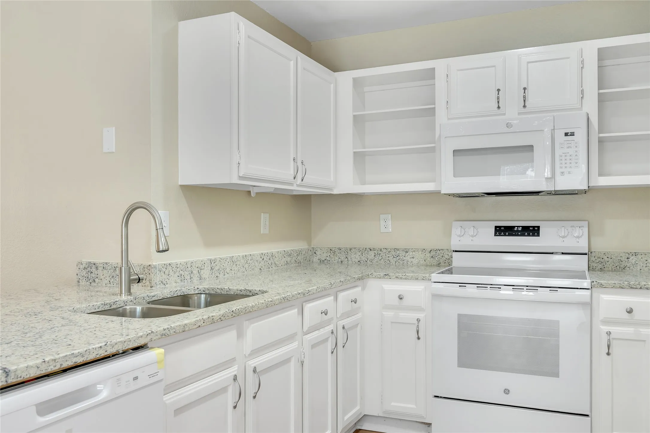 Kitchen featuring white cabinetry, light-colored countertops, stainless steel double basin sink, stainless steel gooseneck faucet, and white appliances