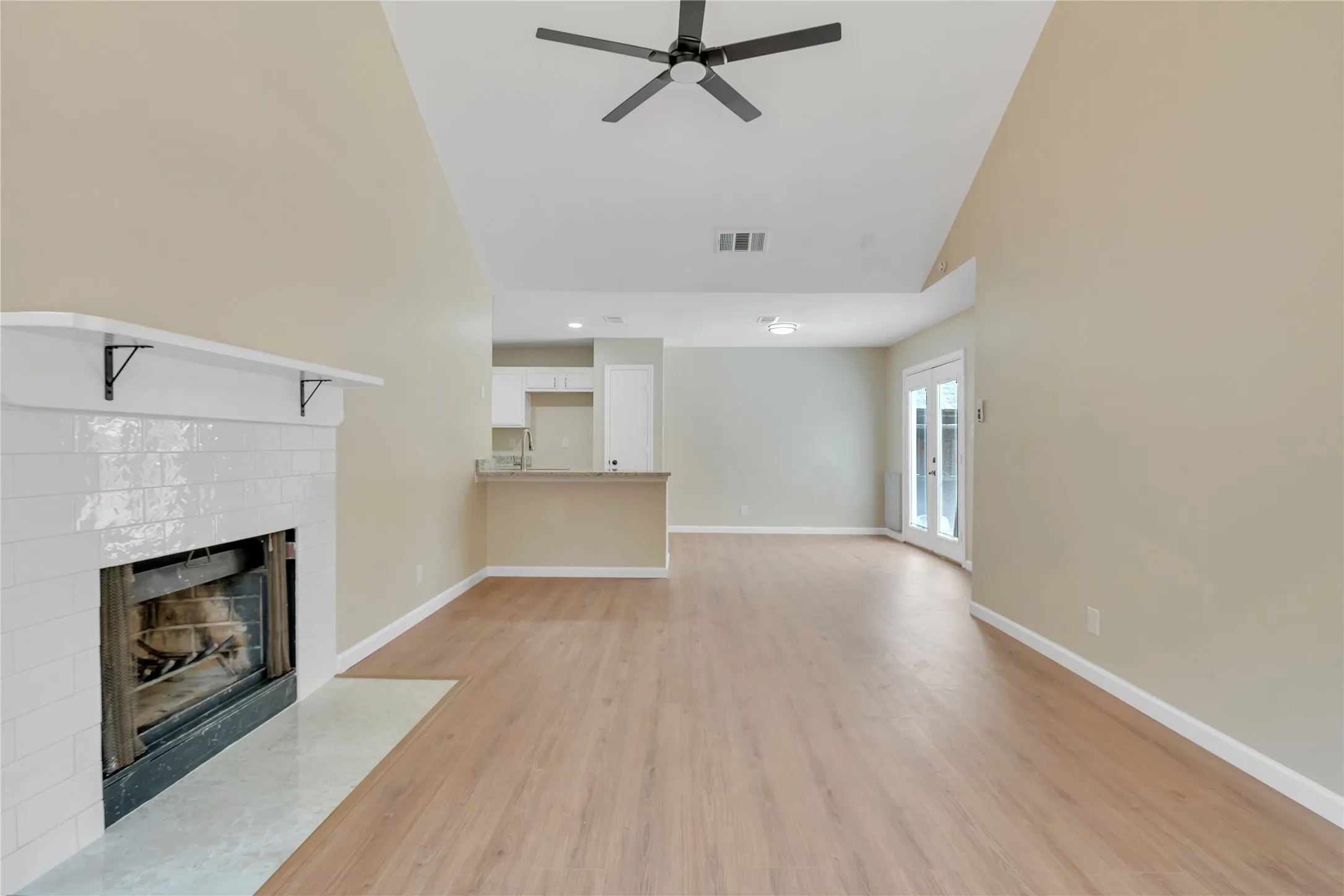 Vaulted ceilings with a ceiling fan, wood-finish flooring, a white tile fireplace, and double French doors with glass panels