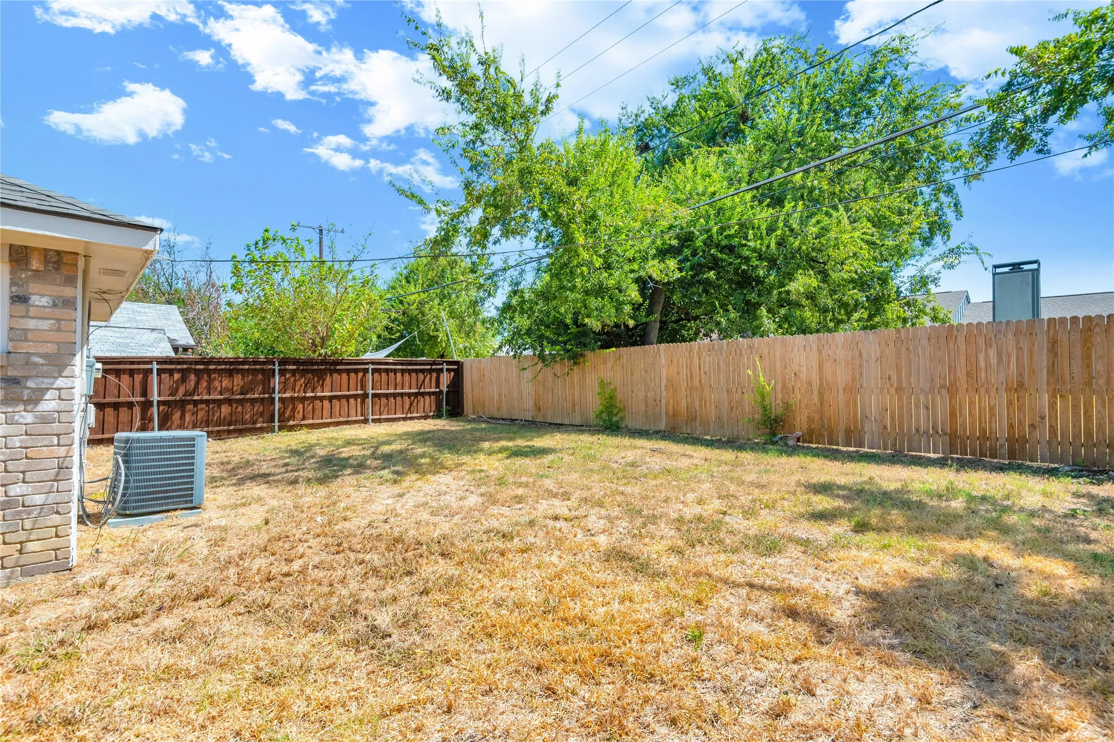 Backyard featuring a wood privacy fence, brick exterior detail, and an air conditioning unit