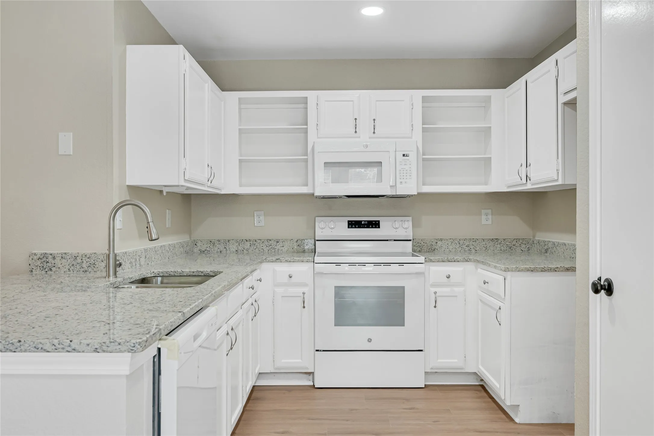 U-shaped kitchen with white cabinetry, speckled countertops, stainless steel sink with gooseneck faucet, and wood-finish flooring