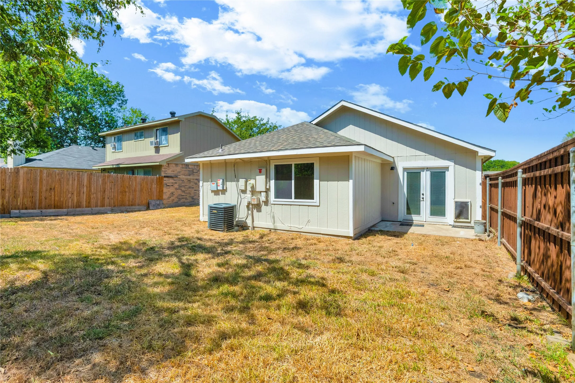 Expansive backyard featuring a wood privacy fence, light-colored siding, and a glass-paned double door
