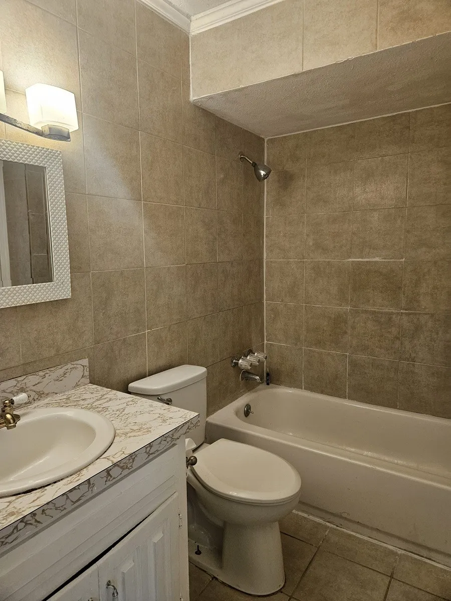 Full bathroom featuring a vanity with an integrated sink, patterned countertop, and white cabinetry