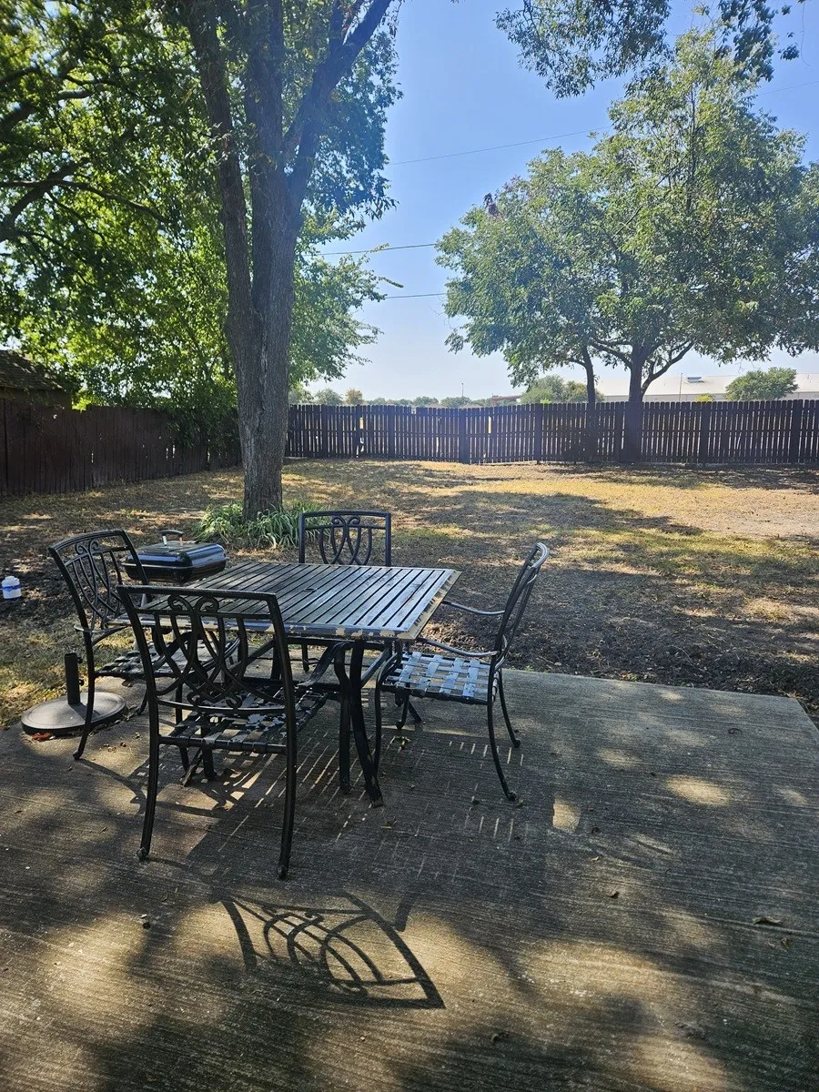 Expansive backyard featuring a concrete patio, mature trees, and a full privacy fence