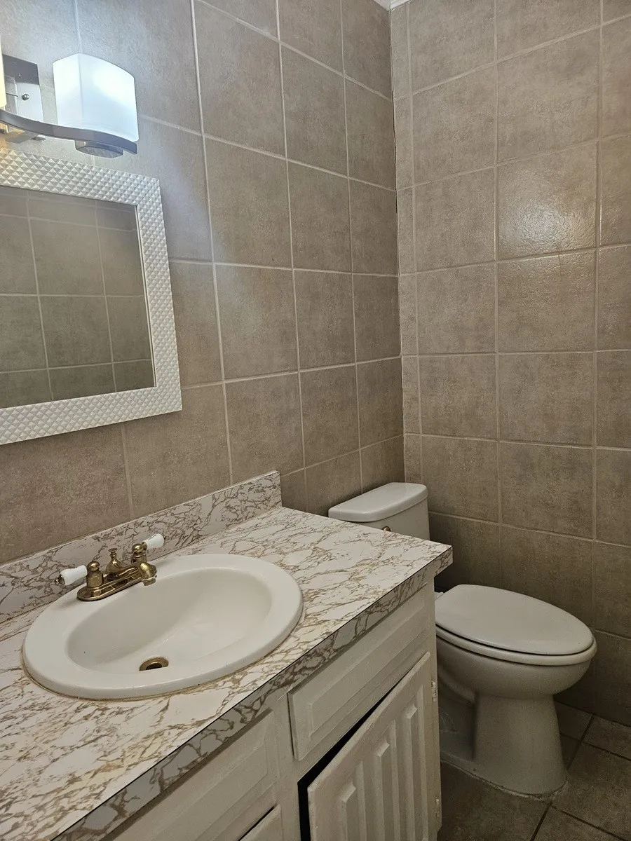 Full-height wall tiling, vanity with integral sink, patterned countertop, and a wall-mounted light fixture