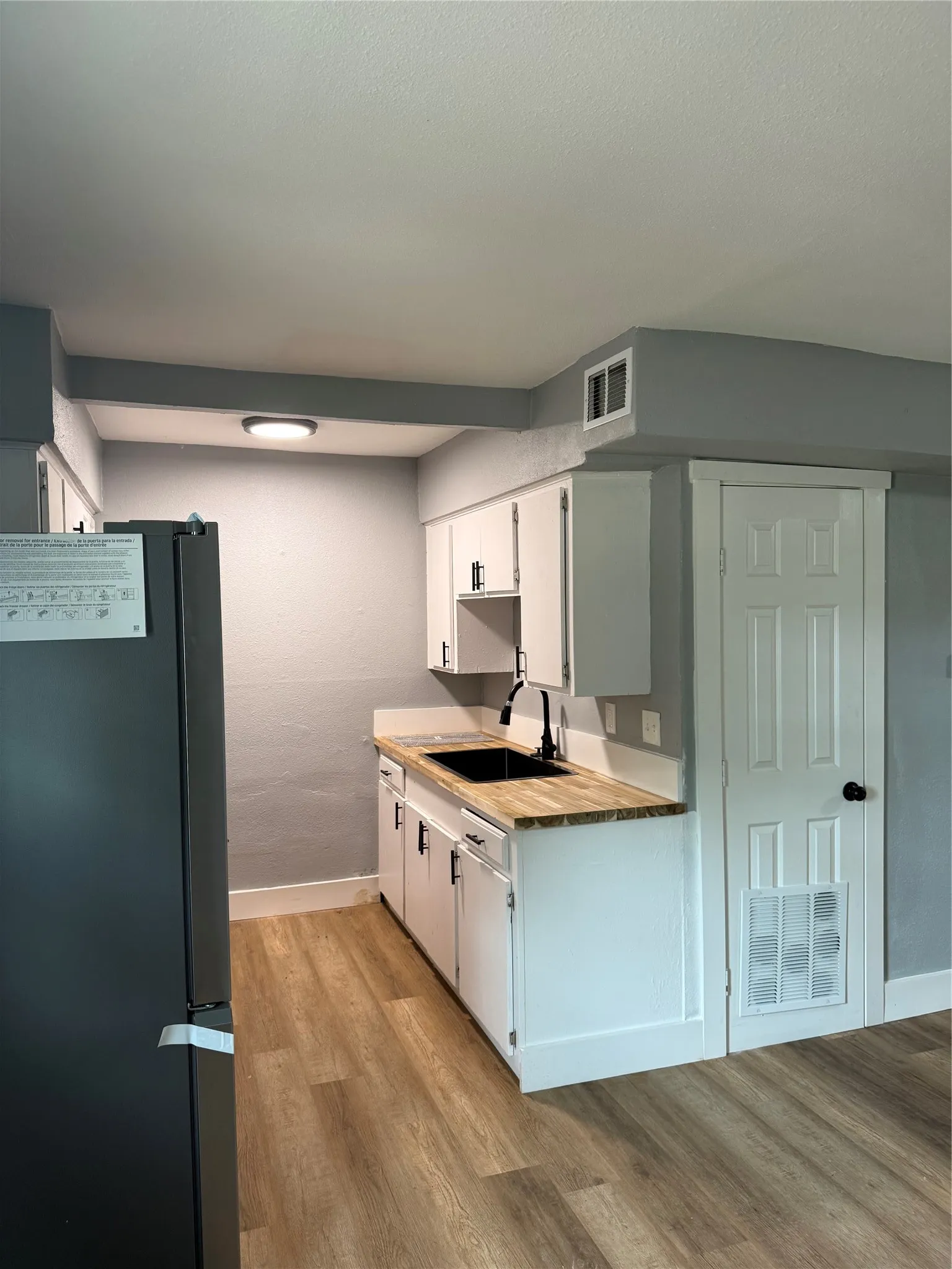 Compact kitchen featuring a black refrigerator, white cabinetry, wood-finish countertops, and wood-finish flooring
