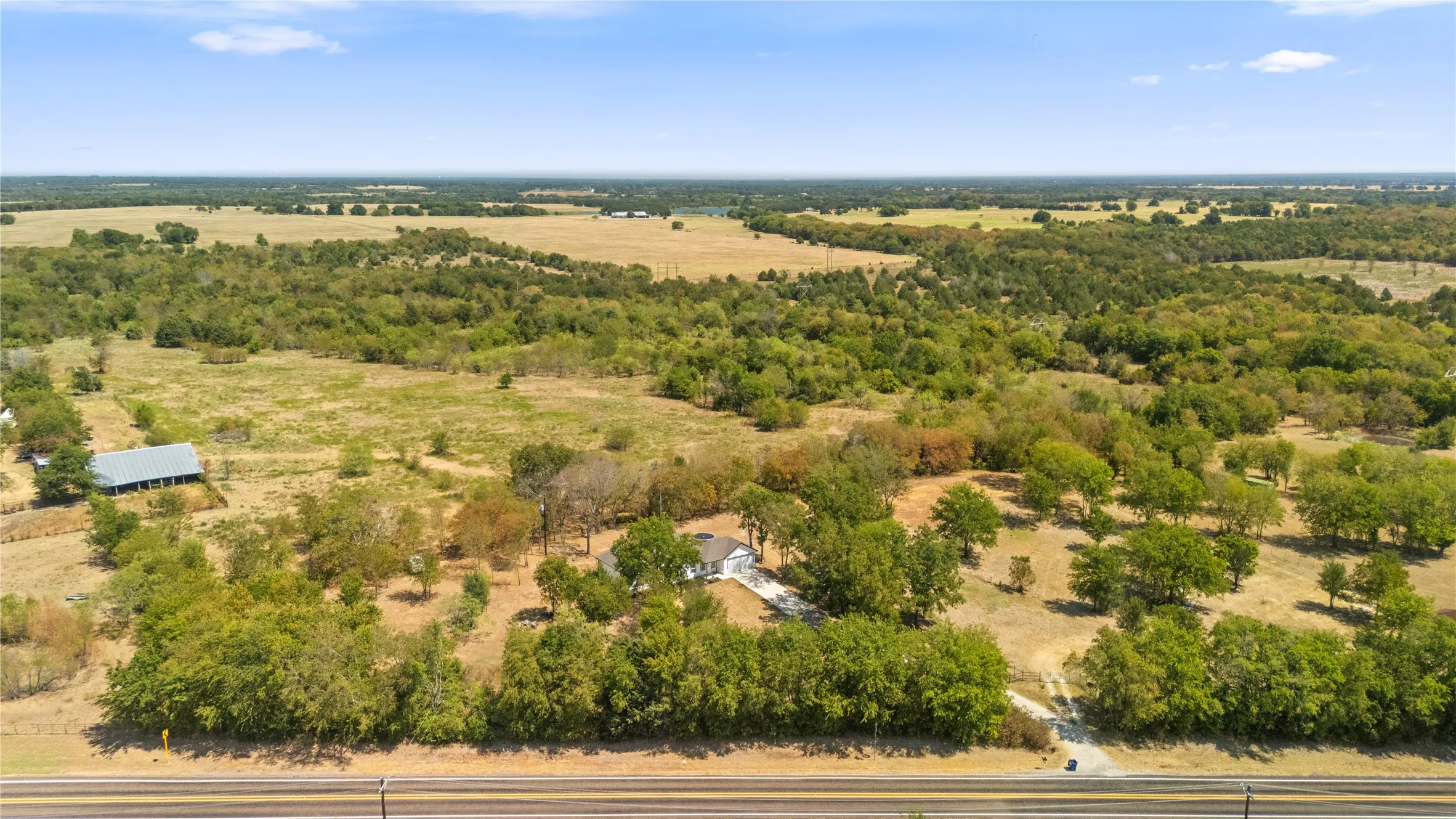 Expansive rural property featuring a single-story residence, mature trees, and open fields