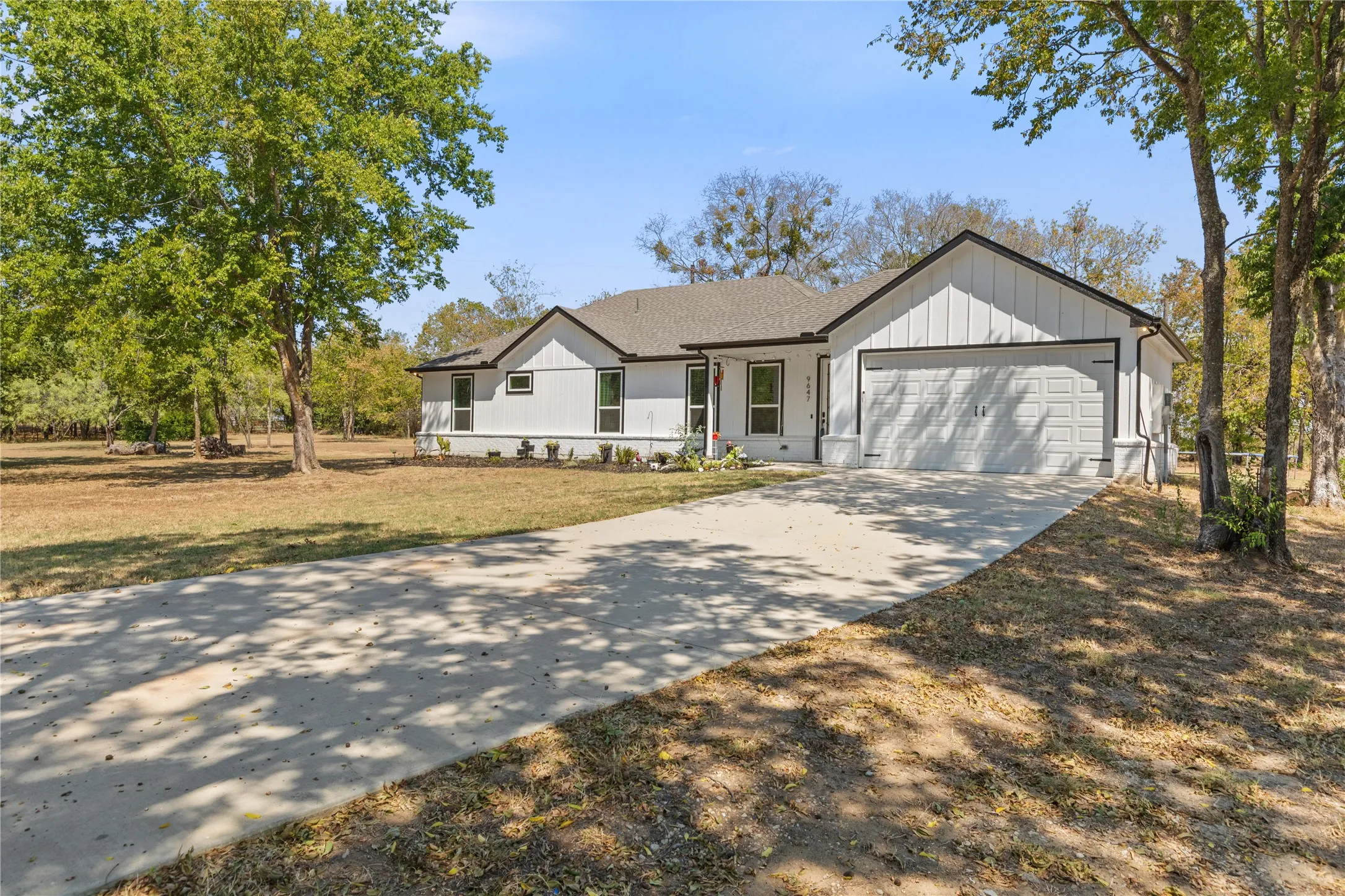 Modern farmhouse-style exterior with vertical siding, attached two-car garage, concrete driveway, and mature trees