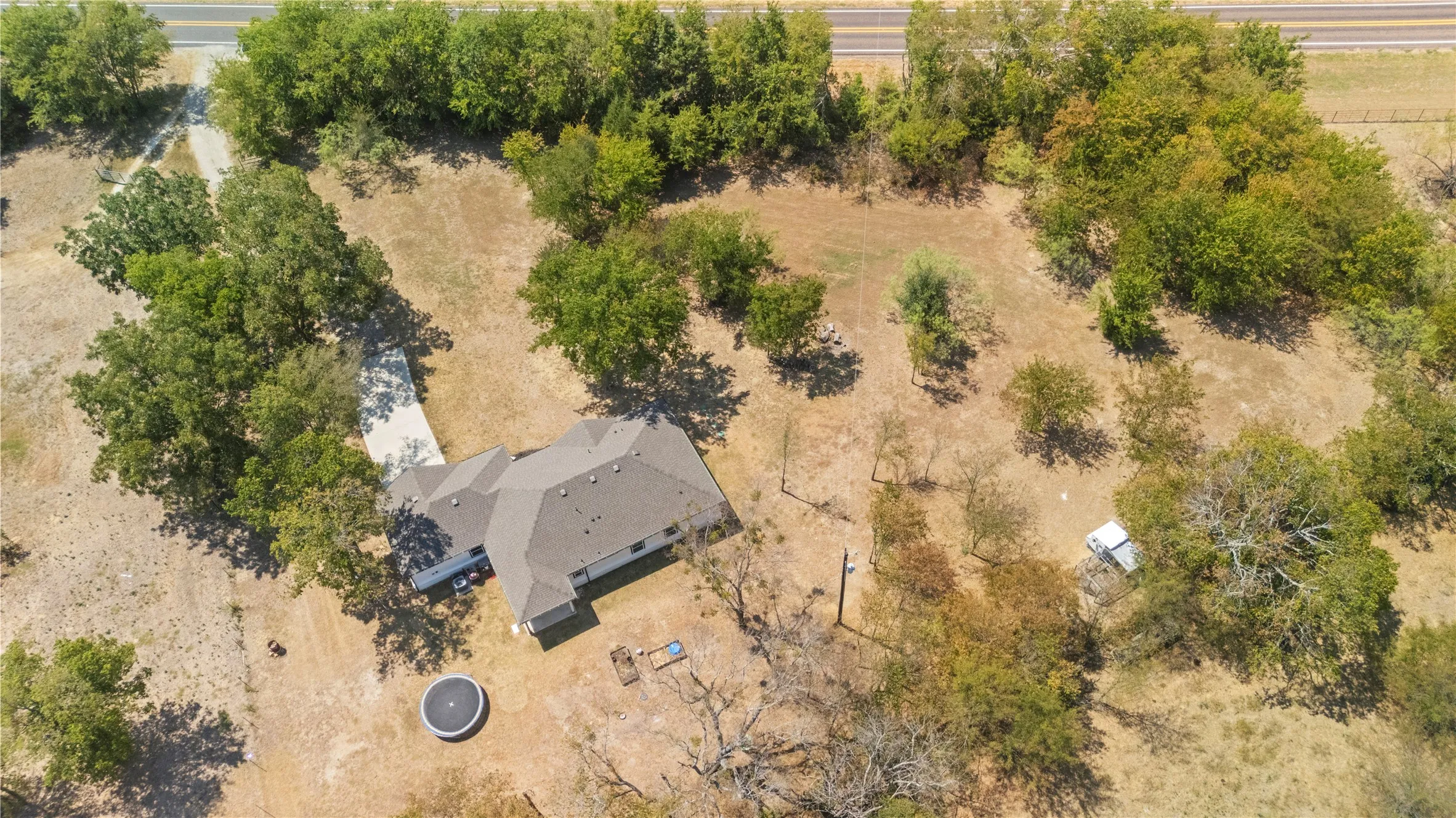 Expansive acreage featuring a single-story residence with a gray shingle roof, mature trees, and a paved driveway