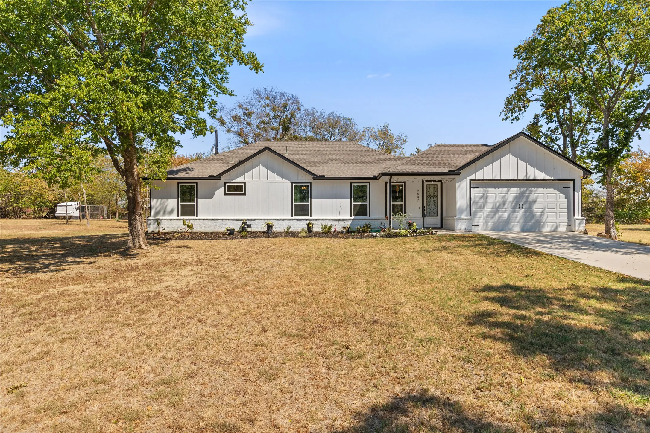 White exterior with vertical paneling accents, attached garage, covered entryway, and mature trees